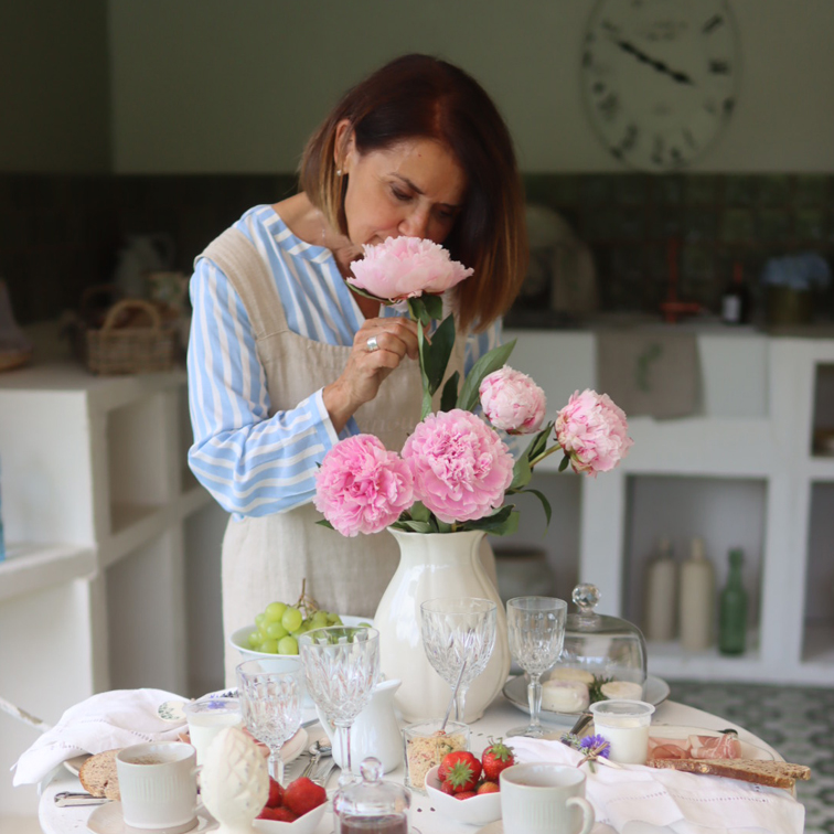 Vrouw in keuken ruikt aan roze pioenrozen in witte vaas op tafel met eten en glazen