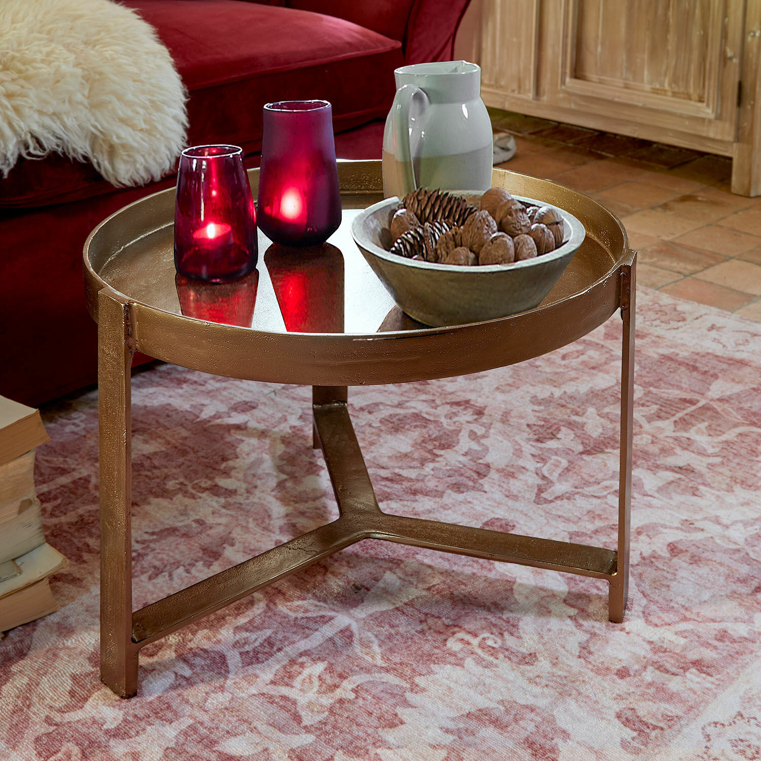 Ronde metalen salontafel in koperen kleur op roze vloerkleed met decoratieve kaarsen en schaal