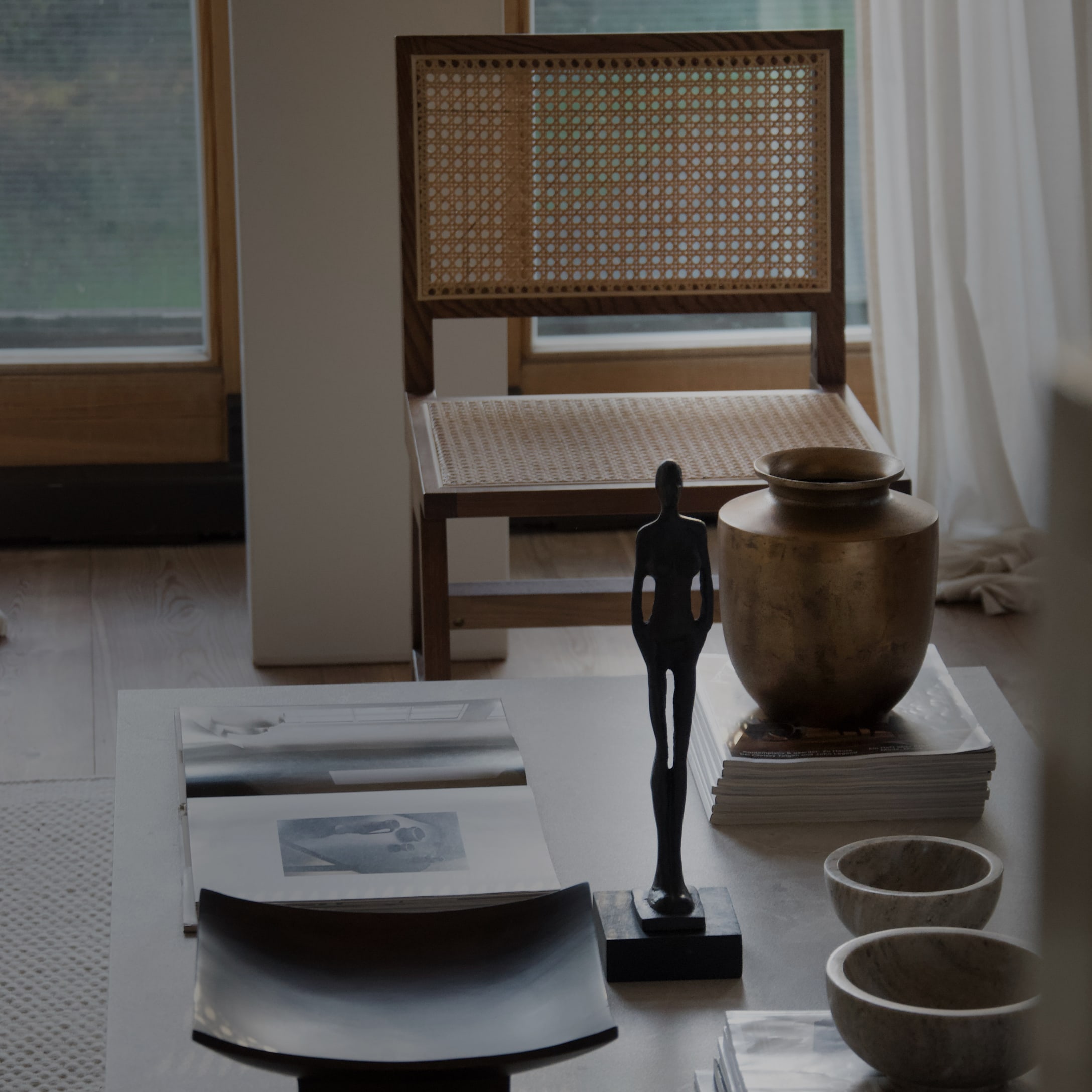 Decoratieve tafel met zwart beeld, messing vaas en rotan stoel op de achtergrond