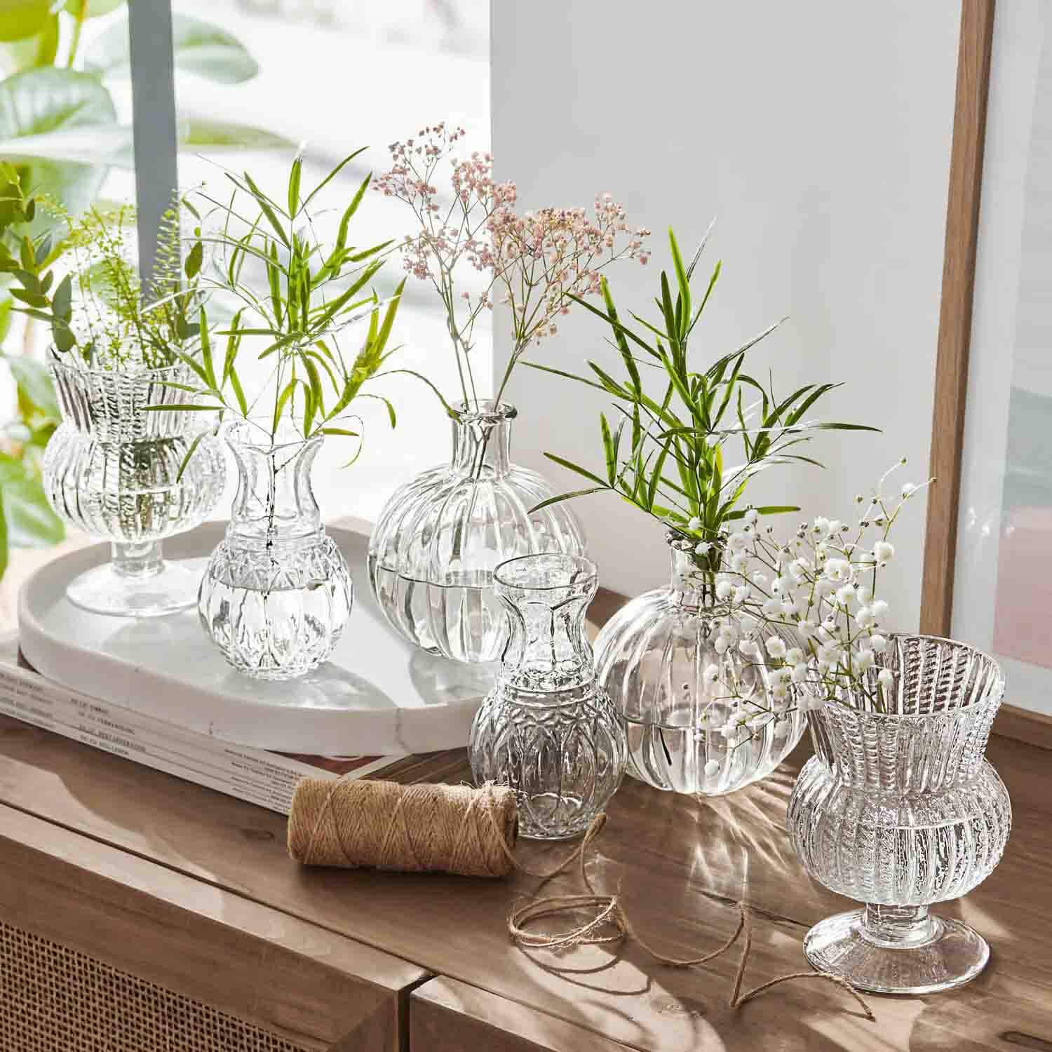 Set transparante glazen vazen met groene en witte bloemen op een houten kast