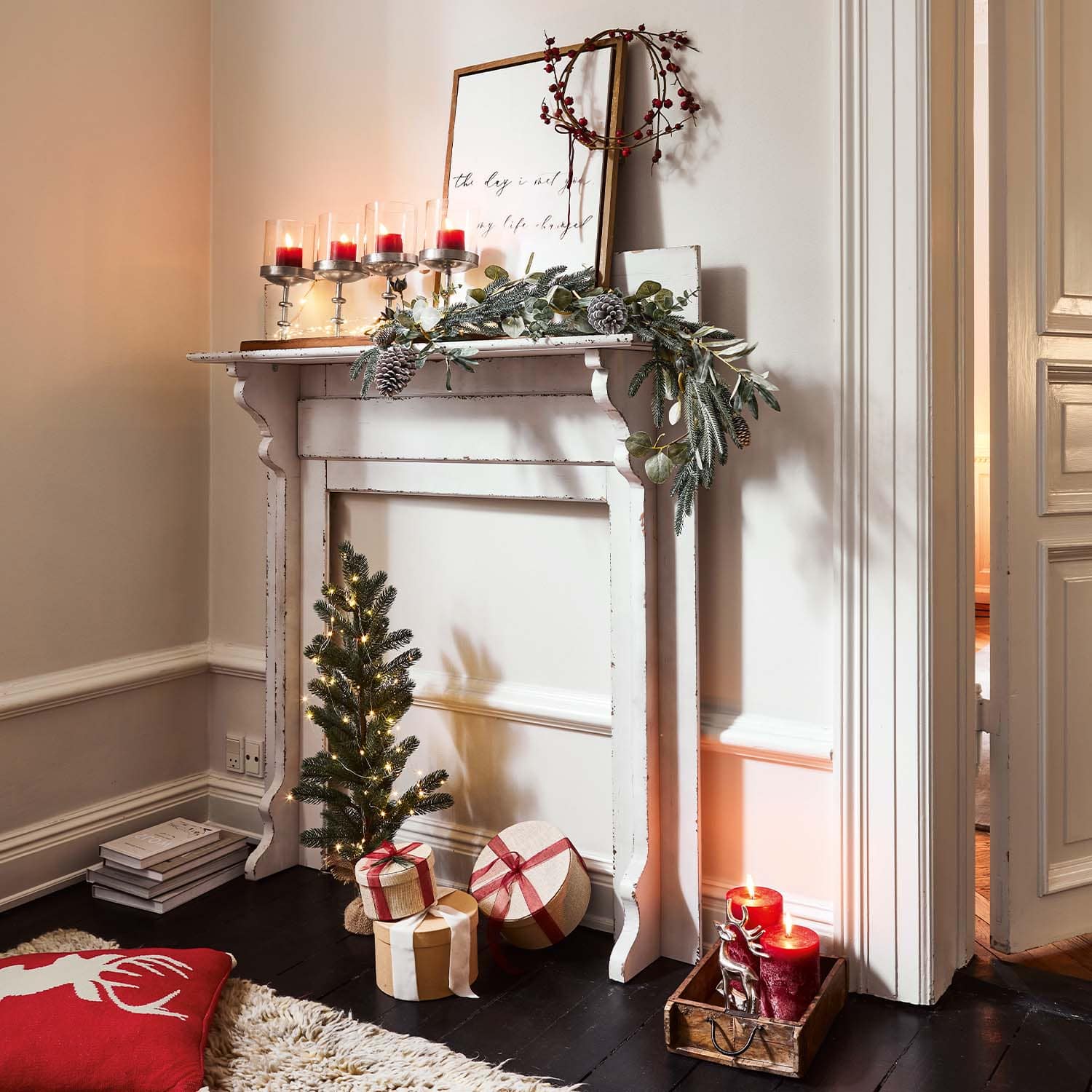 Witte houten schoorsteen met kerstdecoratie, rode kaarsen en verpakte cadeaus op de vloer