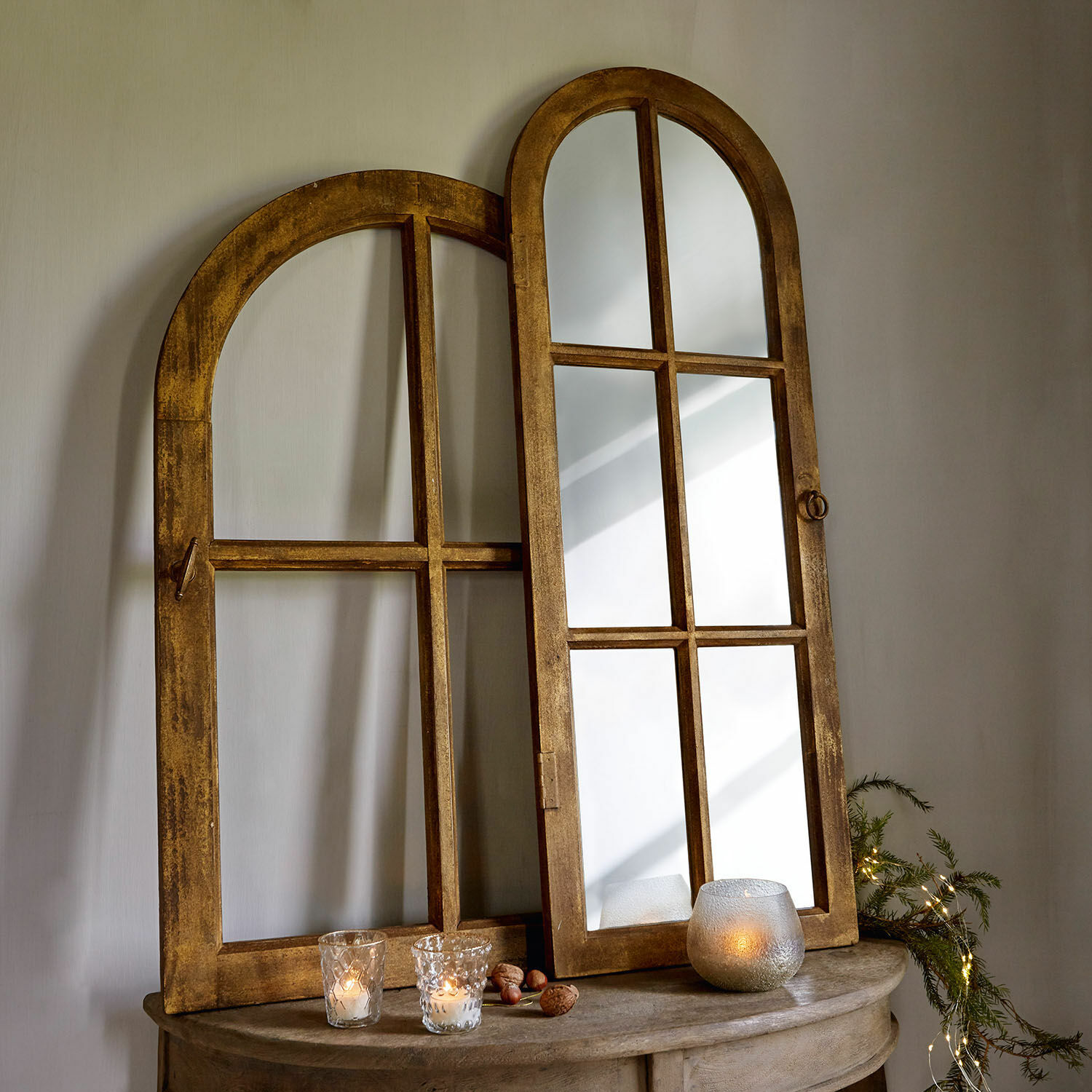 Houten spiegel met afgeronde honingbruine lijst op tafel met kaarsen en natuurlijke decoratie