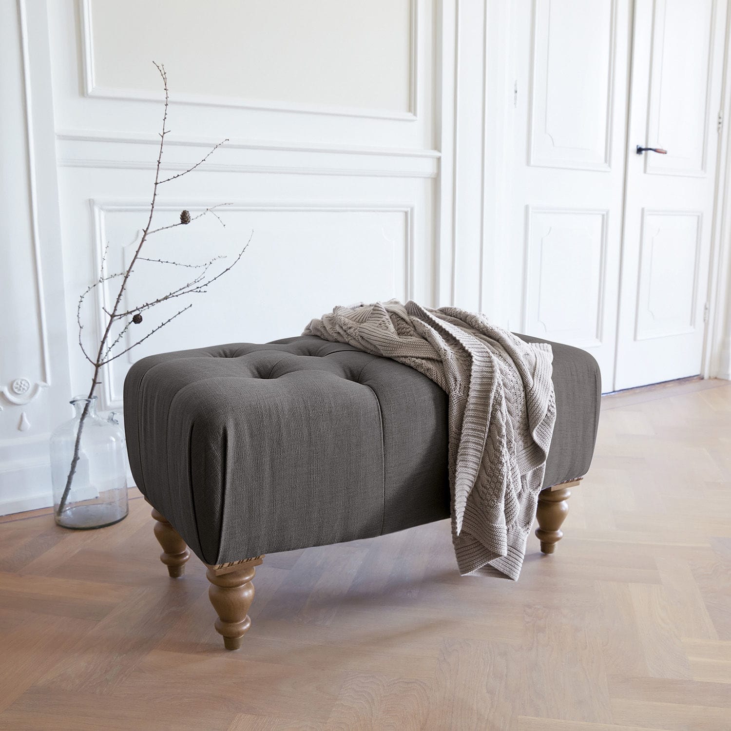 Hocker Durance Grijze gestoffeerde poef met houten poten en beige deken in lichte kamer
