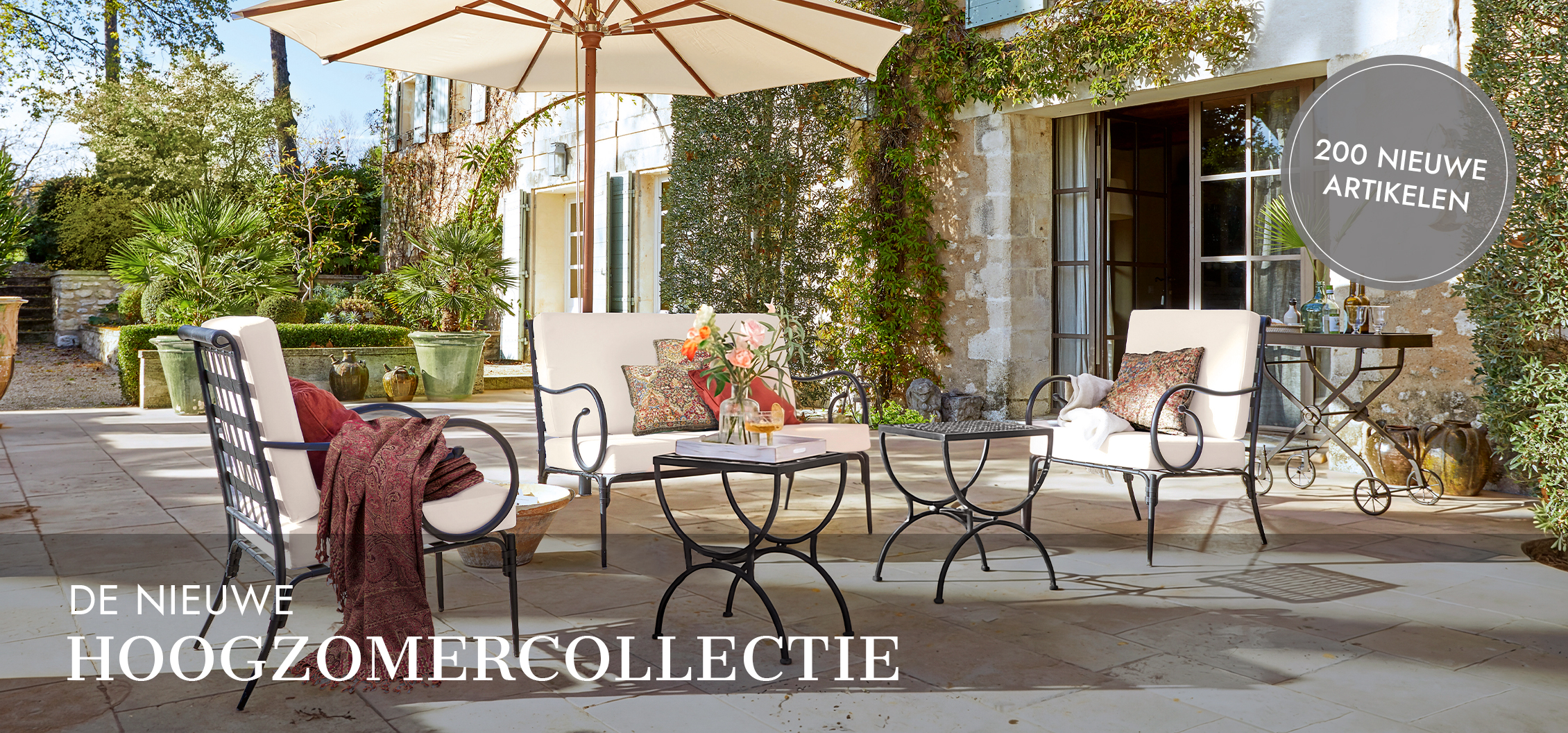 Tuinmeubelset met metalen frame en crèmekleurige kussens onder parasol op stenen terras