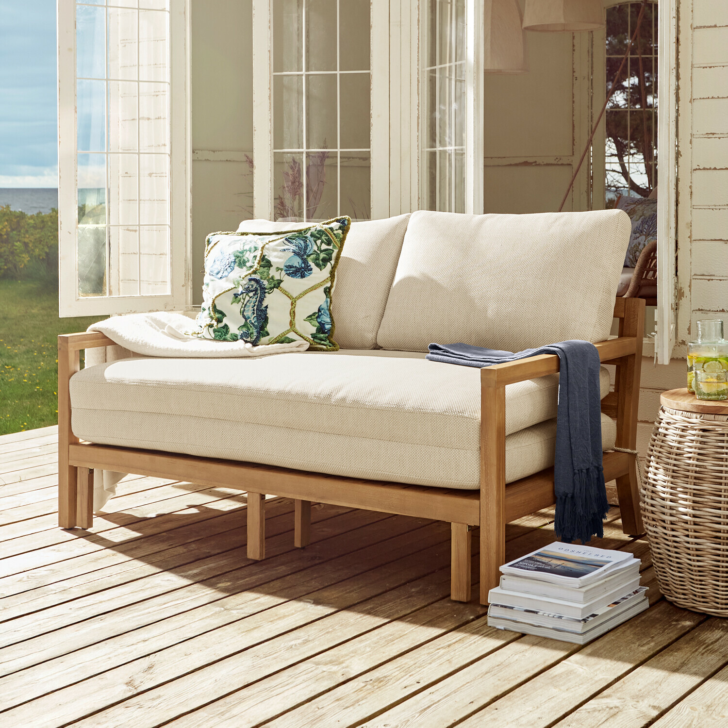Beige bank met houten frame op terras, decoratief kussen en blauwe deken, tuinmeubilair