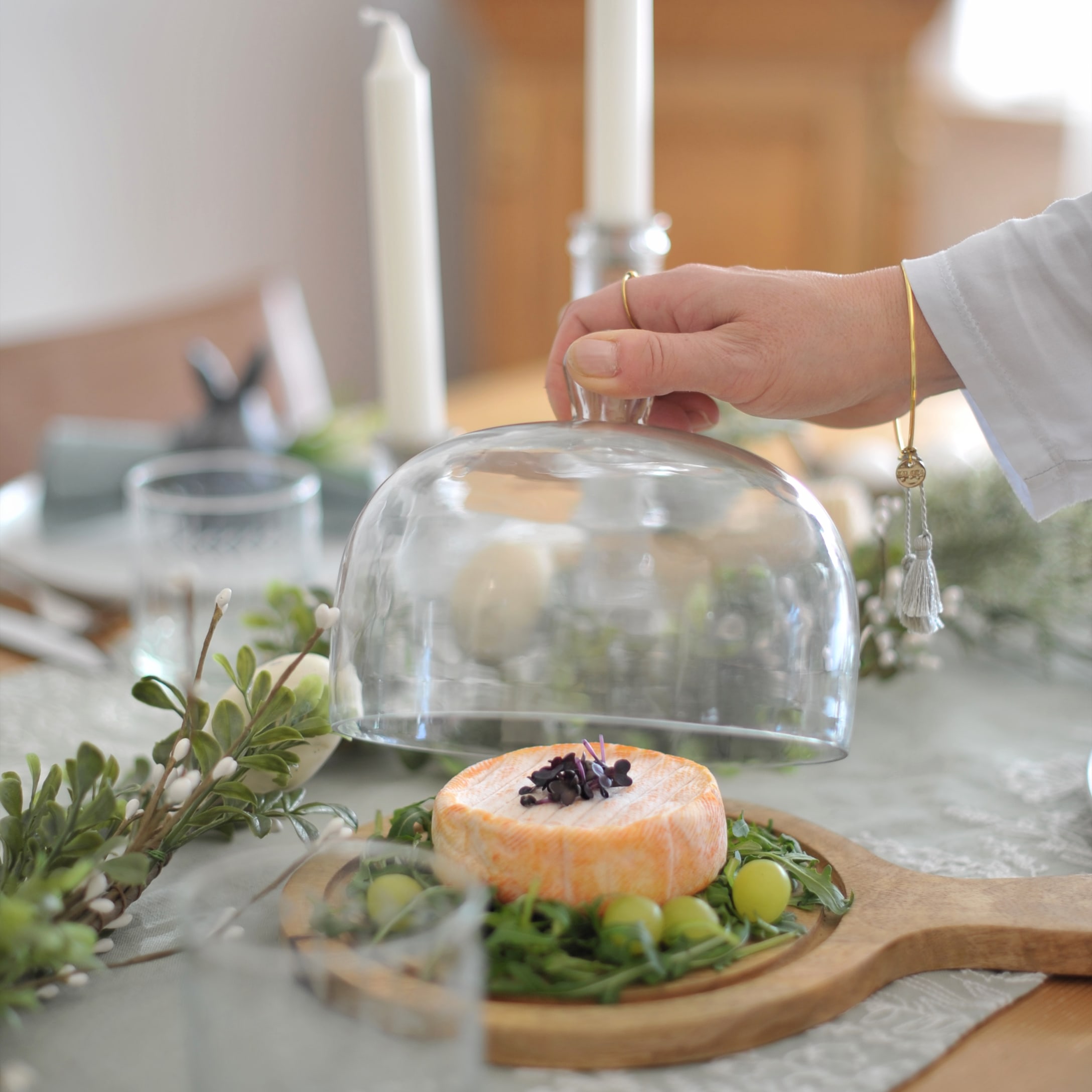 Zachte kaas op houten plank met groene bladeren en druiven onder glazen stolp op tafel