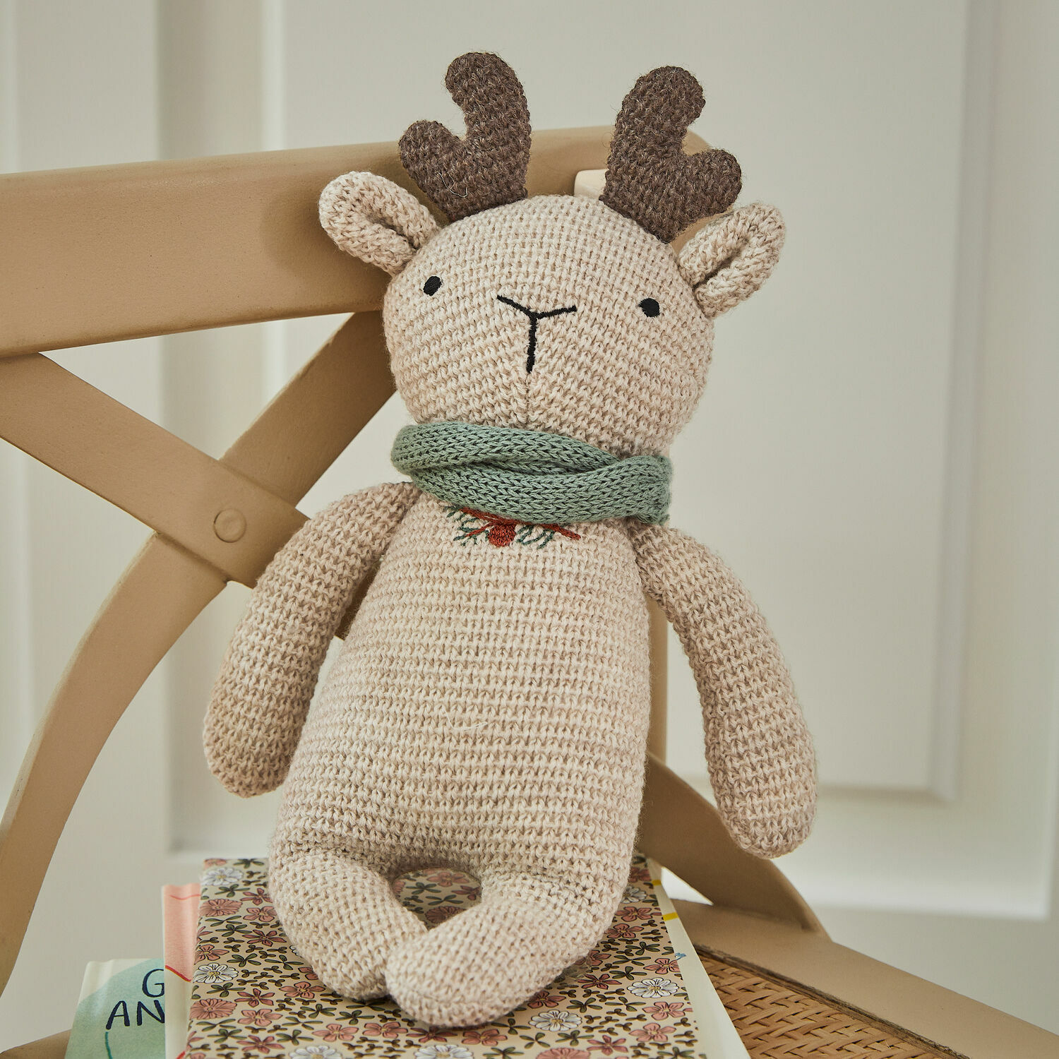 Knuffeldier Papillia Beige gebreide rendierknuffel met bruine hoorns en groene sjaal op stoel