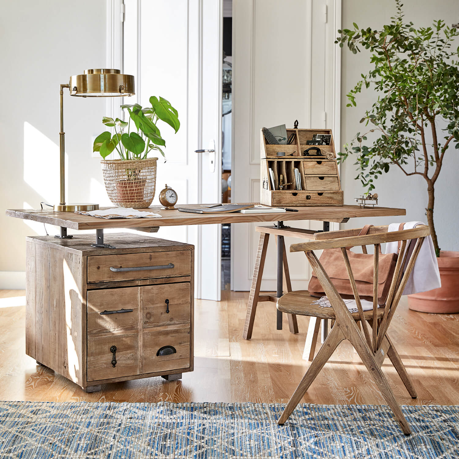 Houten bureau met laden en metalen handgrepen, gouden lamp en plant in gevlochten mand