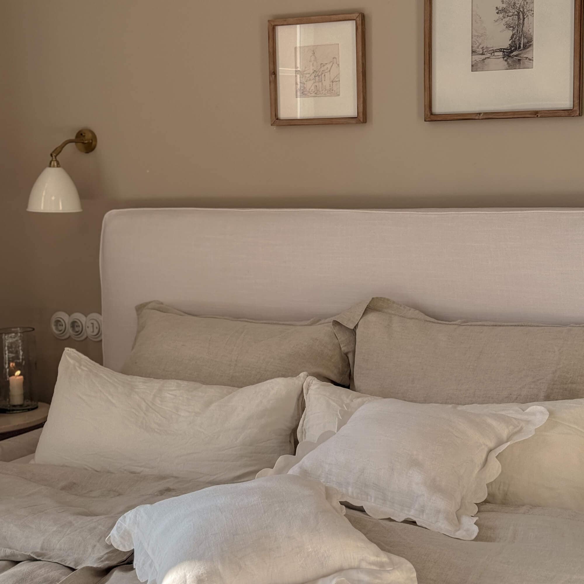 Gezellige slaapkamer met beige linnen beddengoed en licht gestoffeerd hoofdeinde