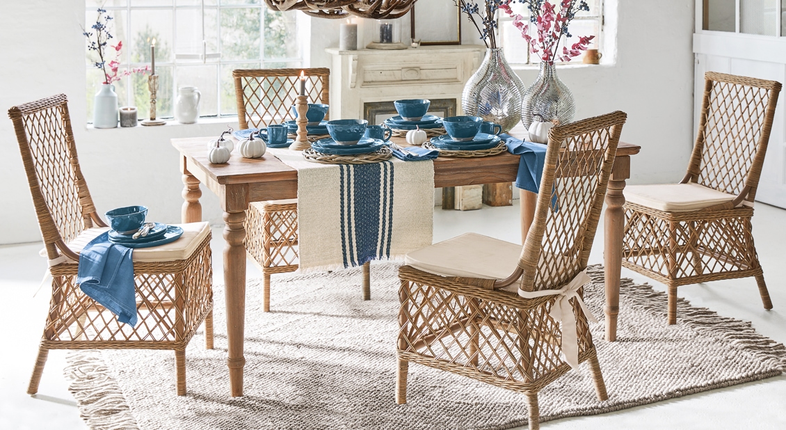 Eetkamer met houten tafel en rotan stoelen met beige kussens en blauw servies