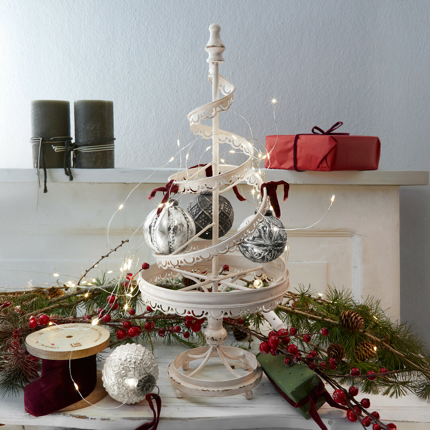 Sierboom Gerzat Witte metalen kerstdecoratie met hangende ballen en LED-lichtjes, rode cadeaus en groene takken op de achtergrond