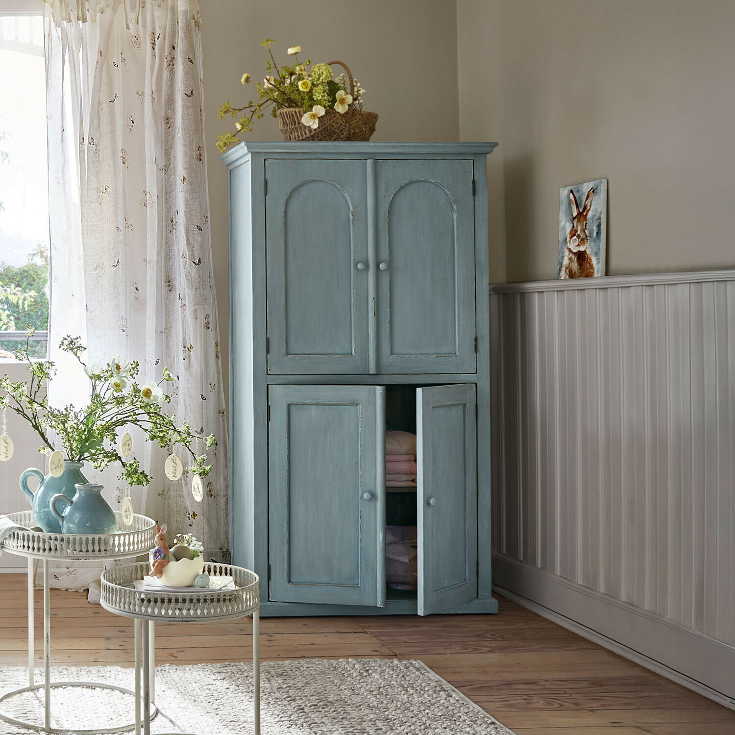 Blauwe houten kast met twee deuren in gezellige woonkamer met lentebloemen en decoratie