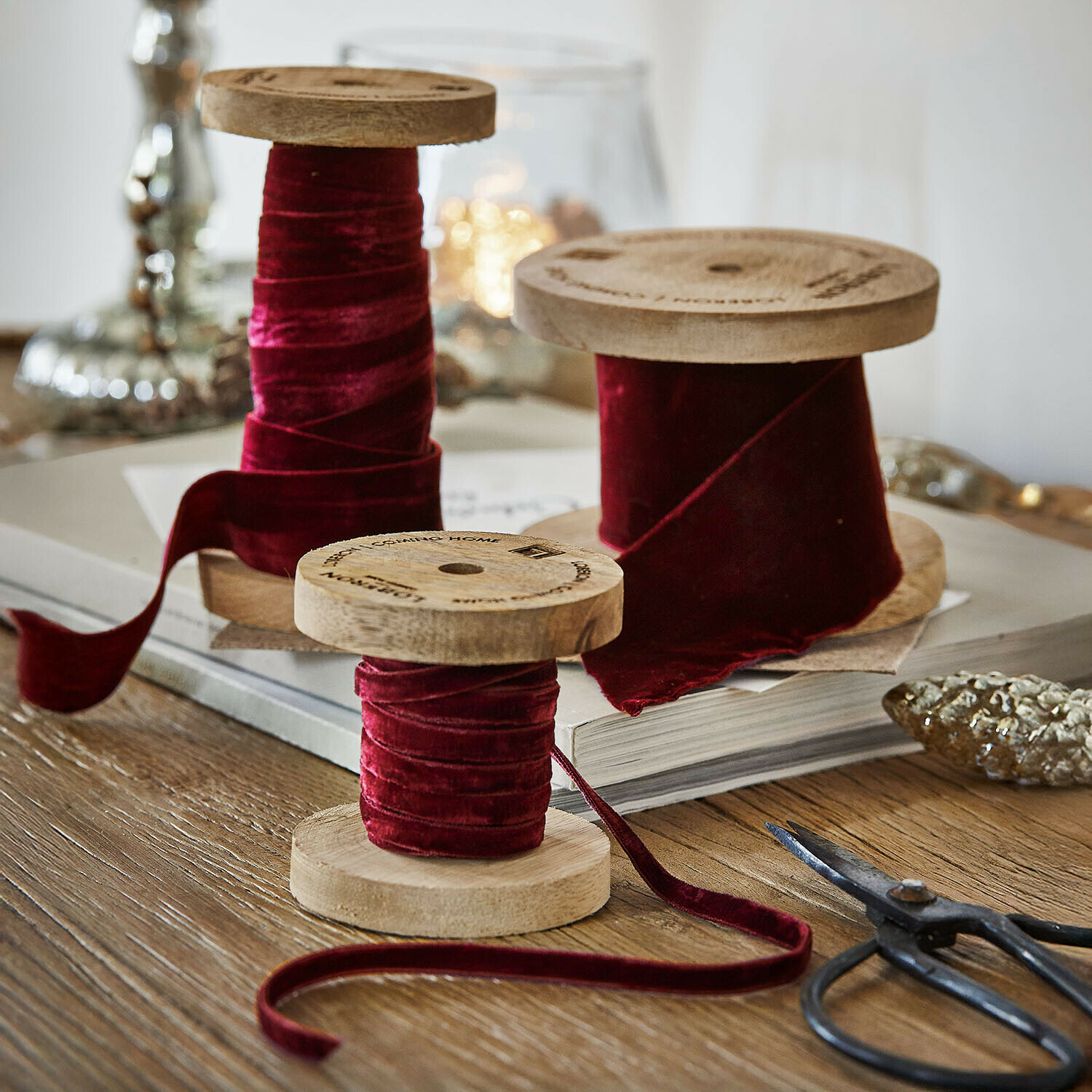 Fluwelen lint set van 2 Liandis Drie houten spoelen met bordeauxrode fluwelen lint op houten tafel met decoratieve schaar