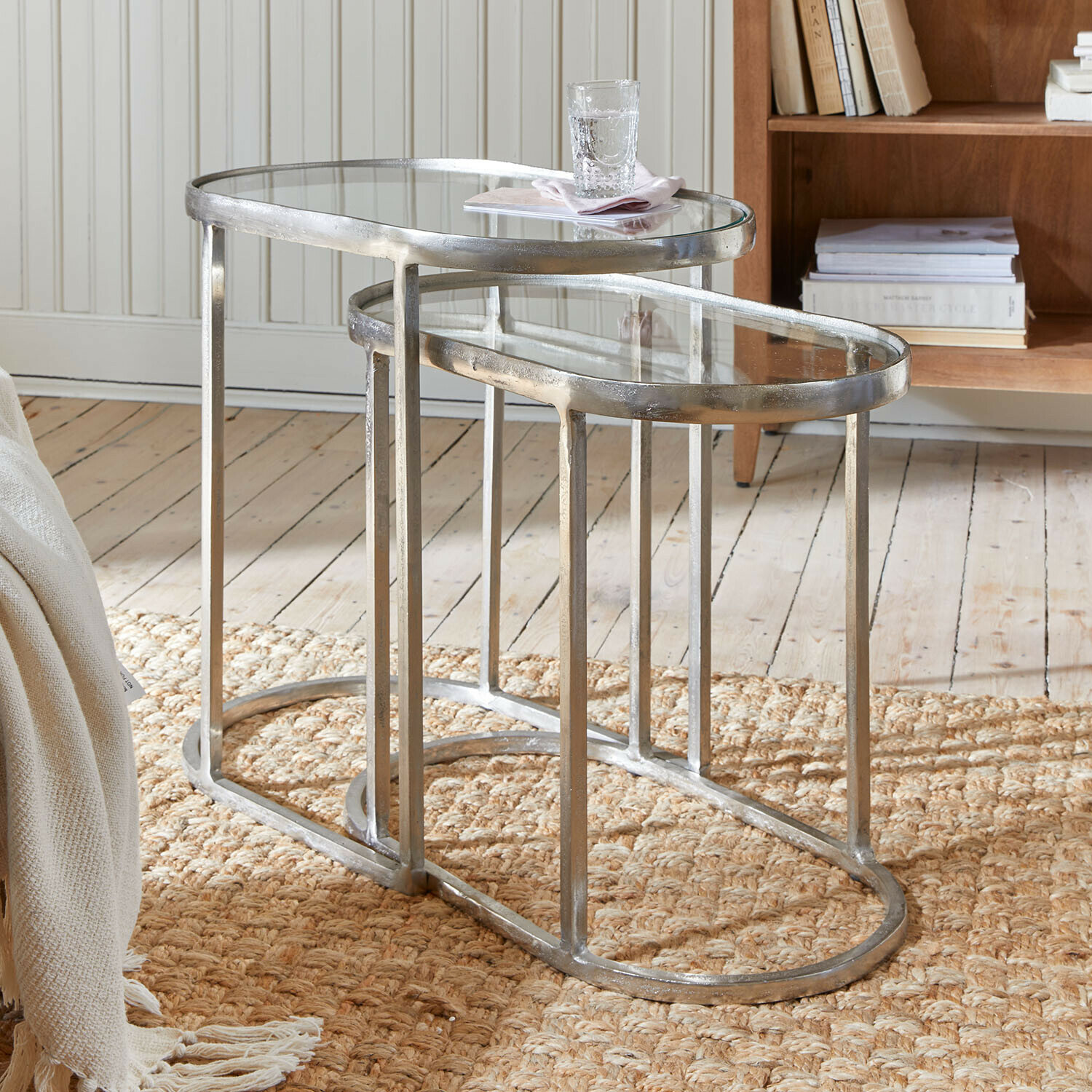 Set van twee bijzettafels met zilverkleurig metalen frame en glazen blad op een geweven vloerkleed