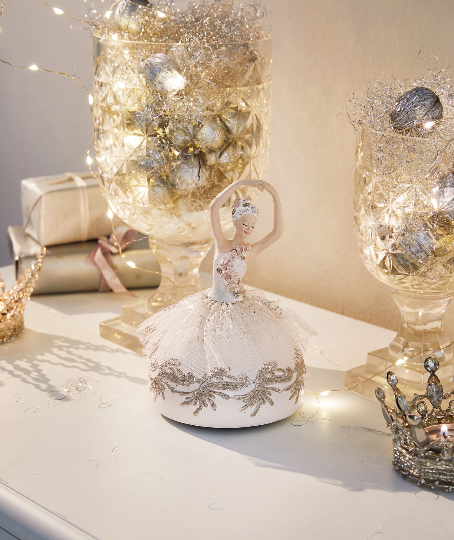 Ballerina-figuur met crèmekleurige stoffen jurk op decoratieve tafel met lichtjes en cadeaus