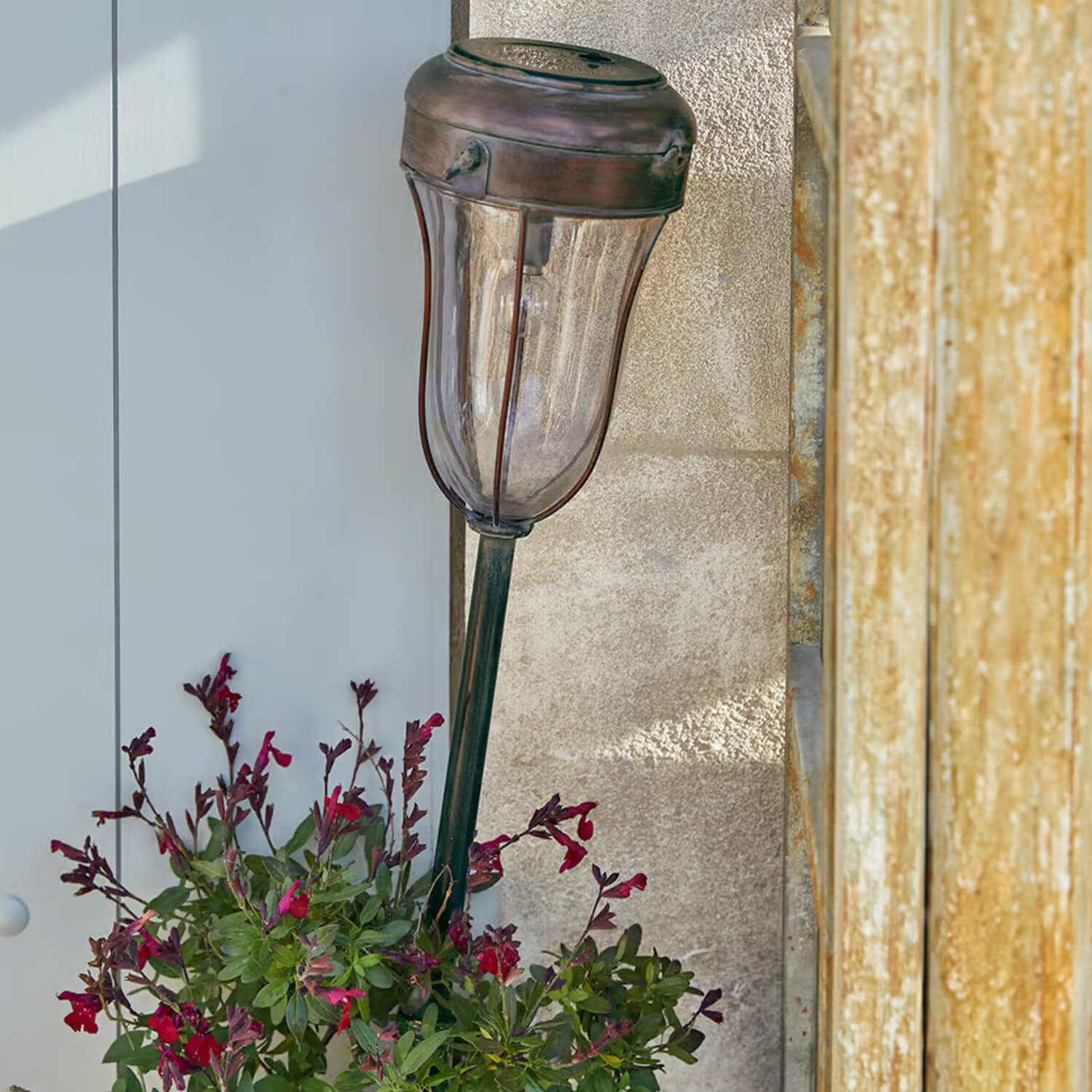 Vintage messing tuinlamp met doorzichtige kap en rode bloemen als decoratie