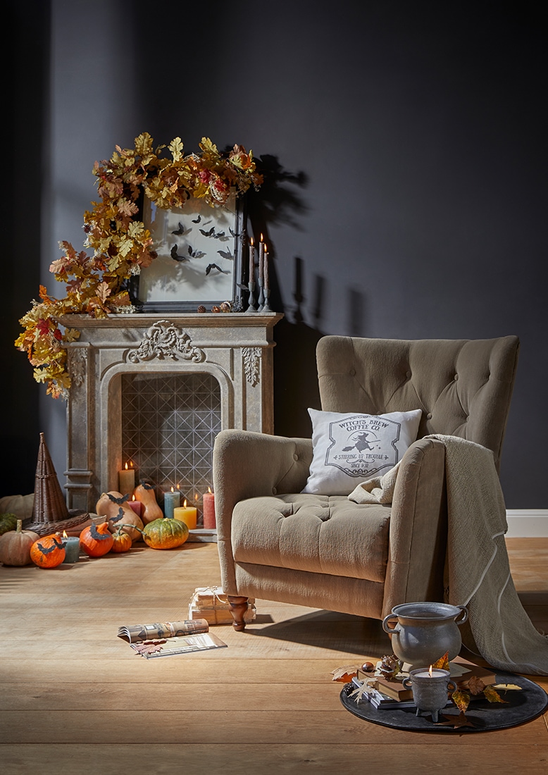 Beige gestoffeerde fauteuil met kussen en deken bij een sierlijke open haard met herfstdecoratie en pompoenen