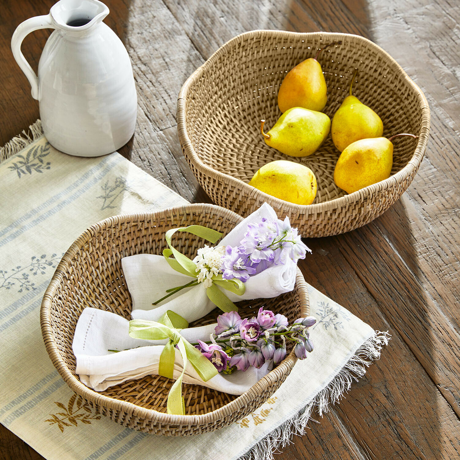 Twee ronde rotan manden op houten tafel, één met peren, de ander met servetten en bloemen