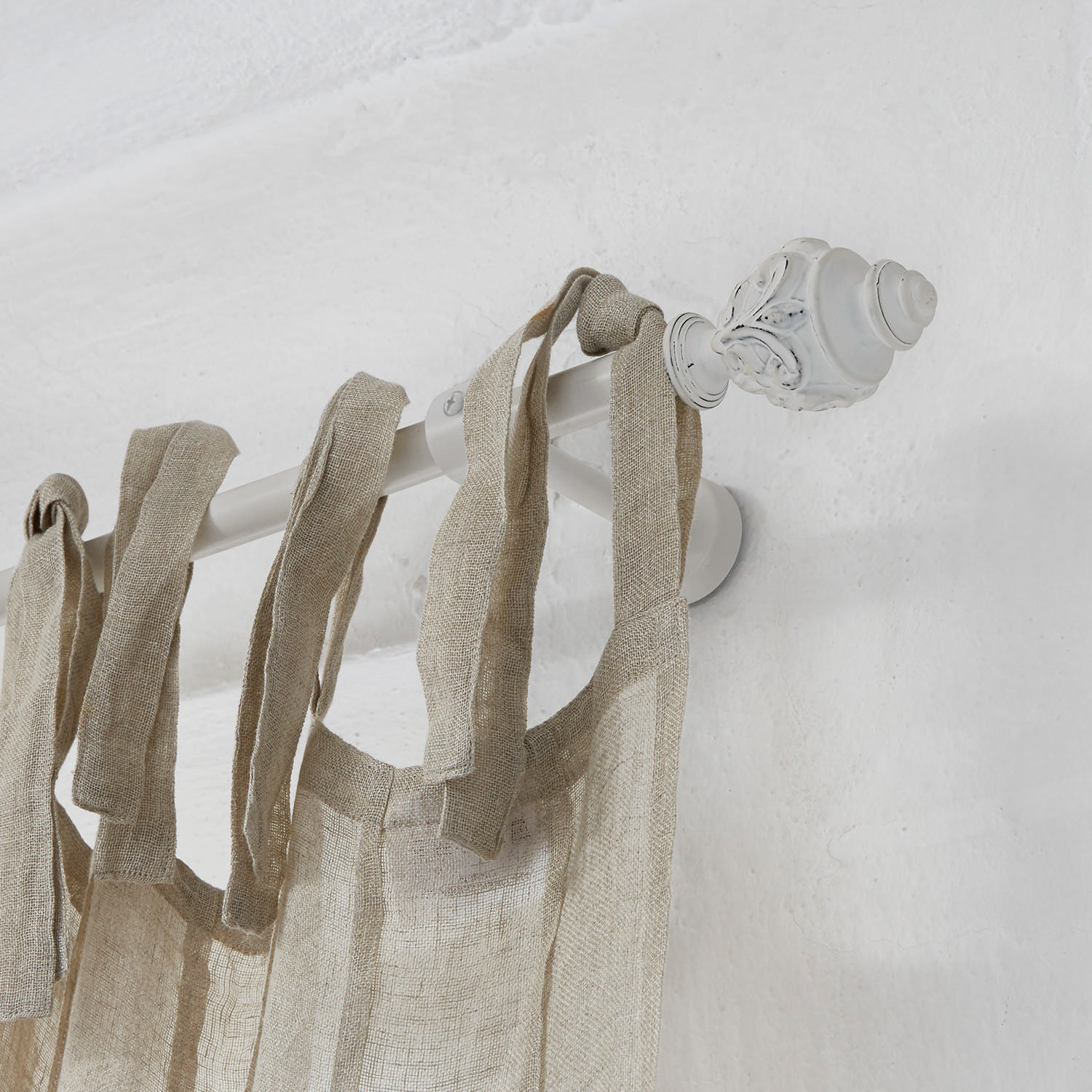 Witte metalen gordijnroede met decoratief uiteinde en natuurlijke linnen gordijn