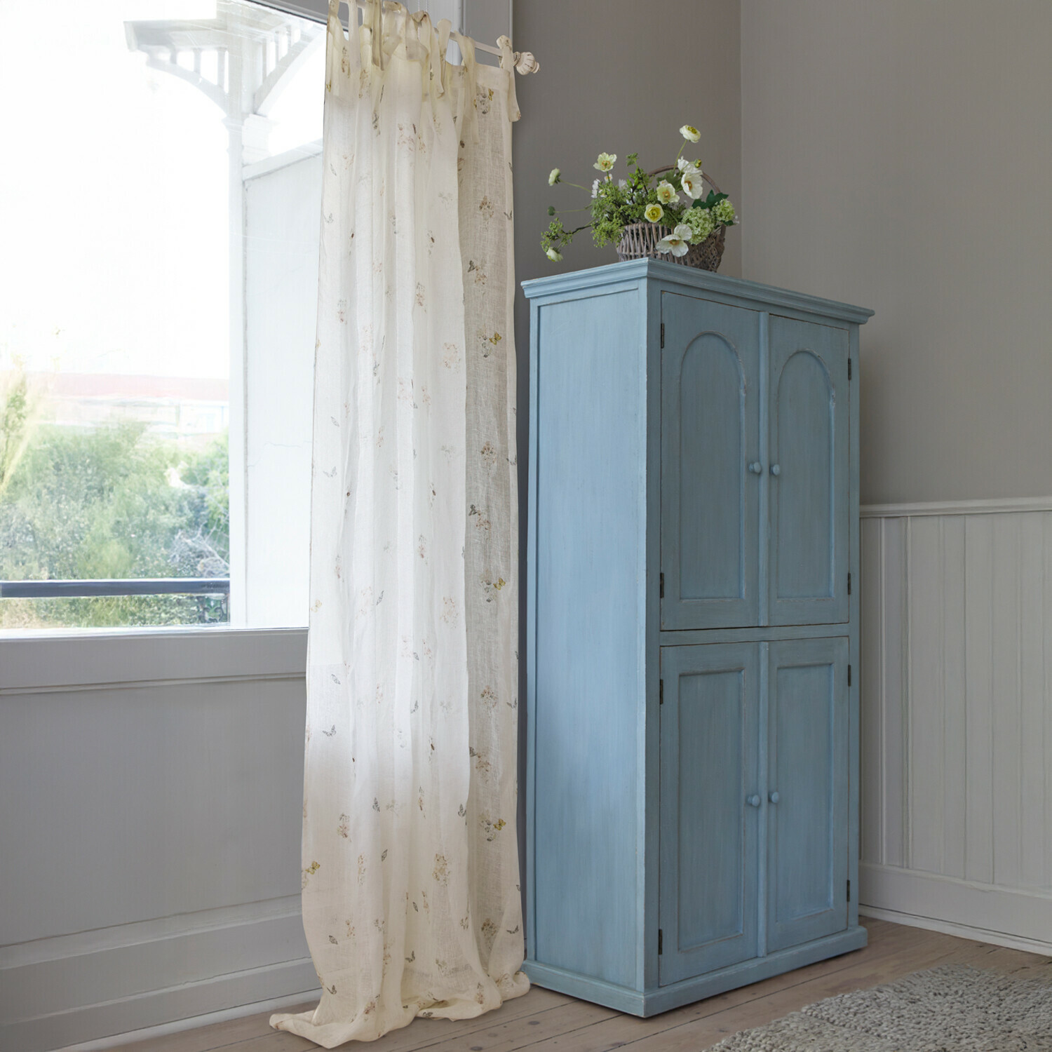 Blauwe houten kast met vier deuren en decoratieve bloemenmand in lichte kamer