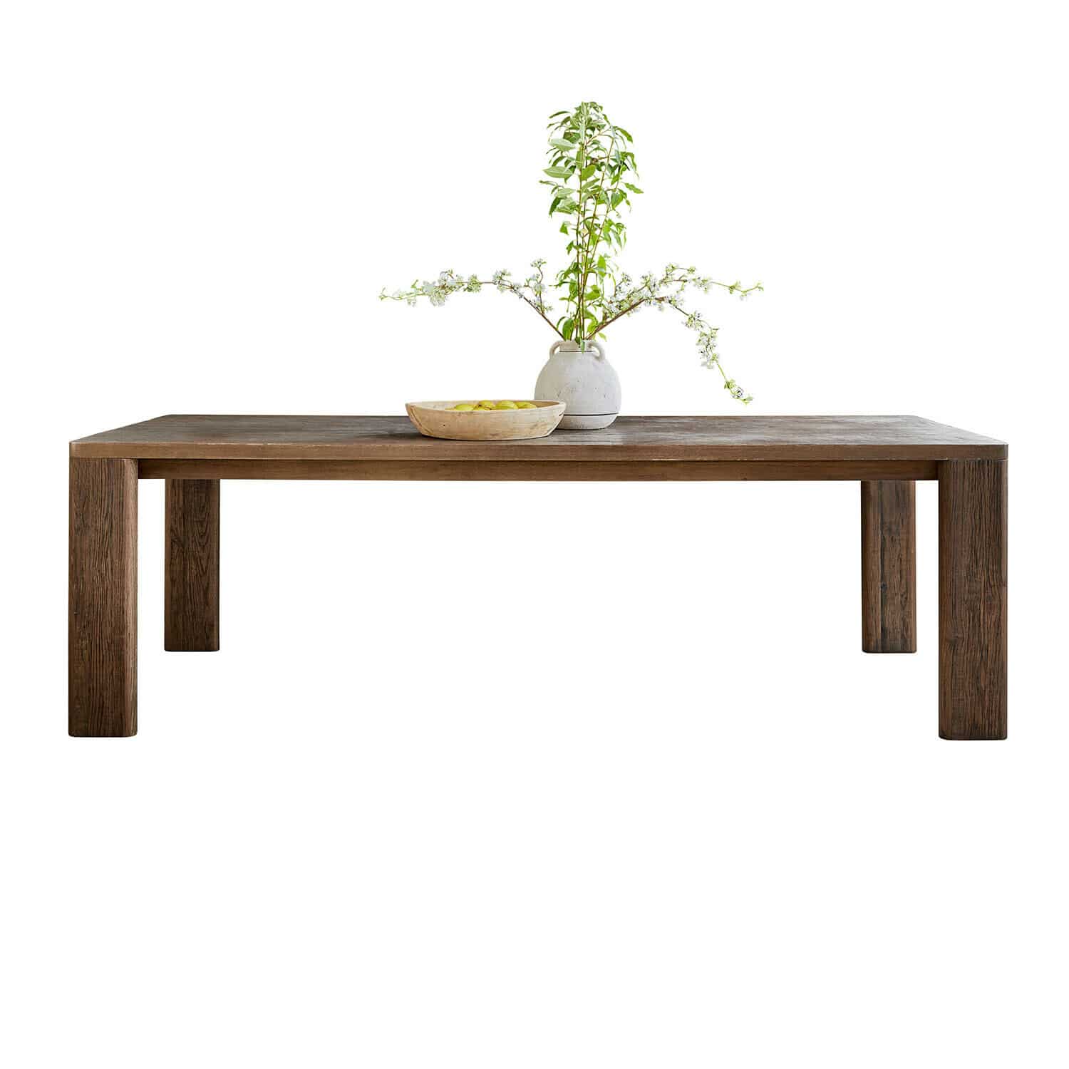 Donkere houten tafel met rechthoekig blad, versierd met keramische vaas met groene takken en schaal met fruit