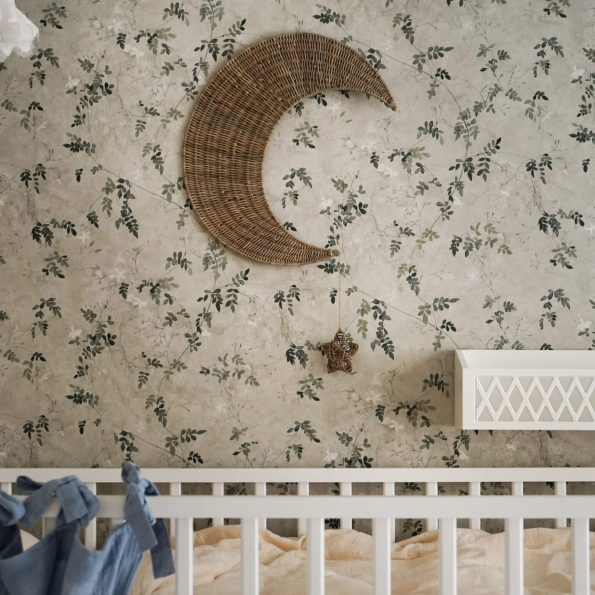 Wanddecoratie maan van riet met hangende ster tegen bloemenbehang in kinderkamer