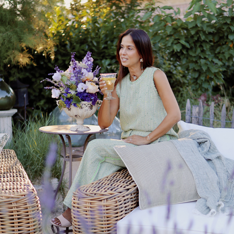 Vrouw in groene jurk zittend op rotan meubel in tuin met bloemenboeket en wijnglas