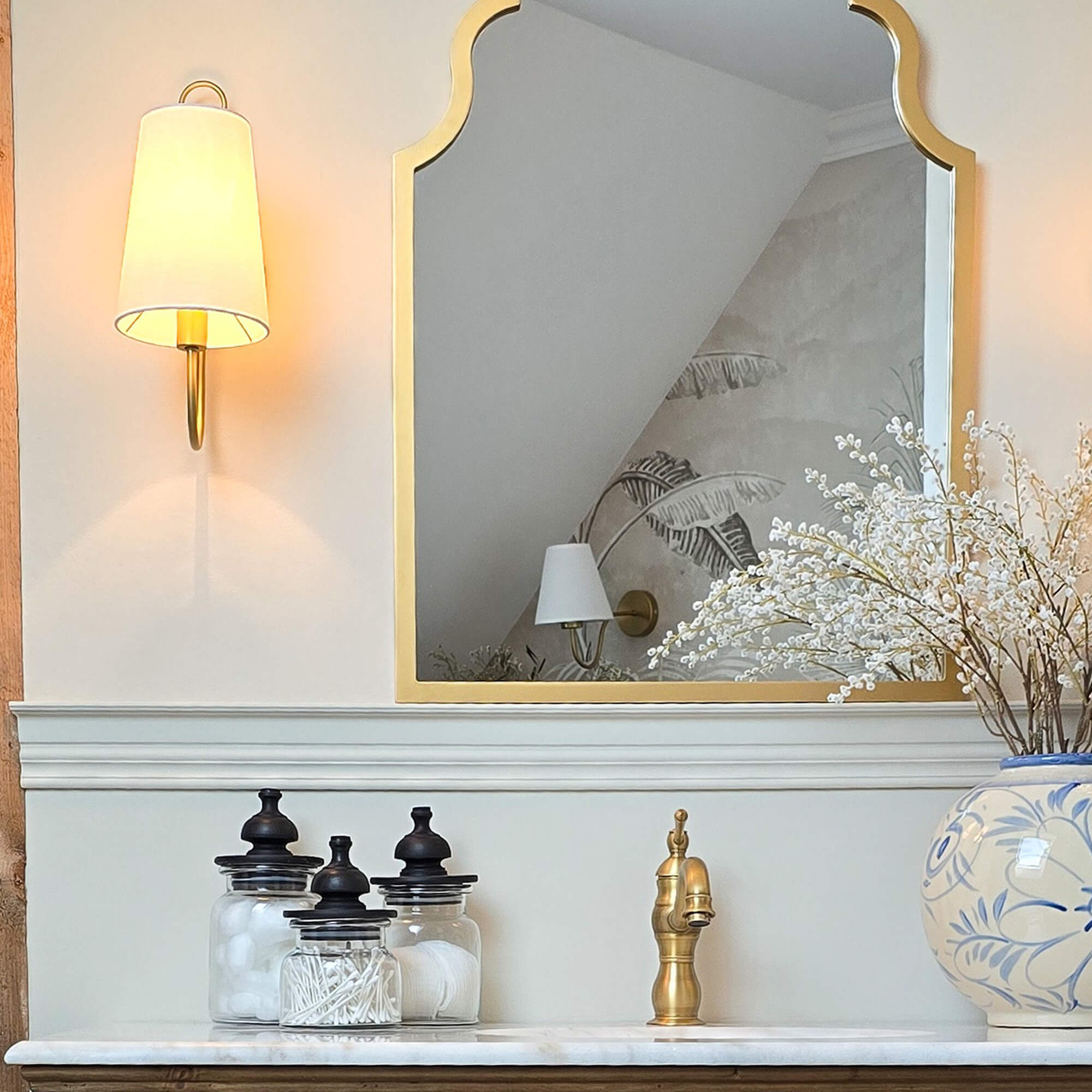 Gouden spiegel met decoratieve lijst boven marmeren wastafel met messing kraan en glazen potten