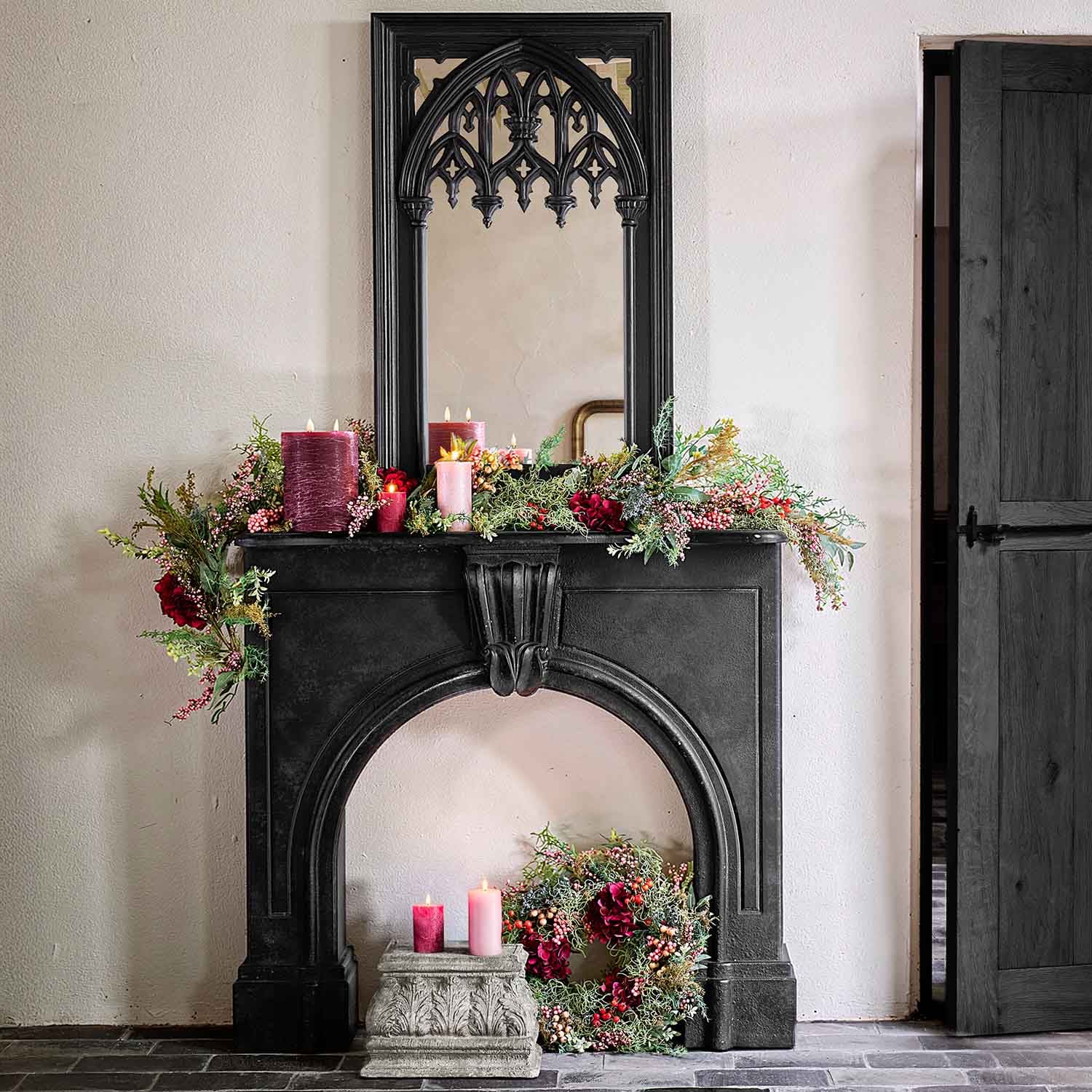 Zwarte decoratieve open haard met gotische spiegel, versierd met rode kaarsen en groene slingers voor interieur