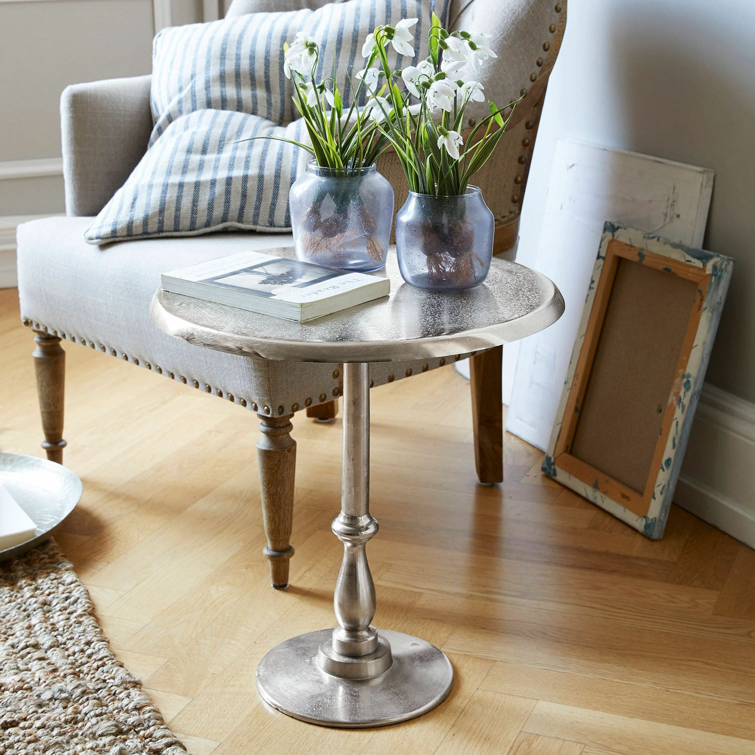 Ronde zilverkleurige metalen bijzettafel met decoratieve vazen en boek in woonkamer