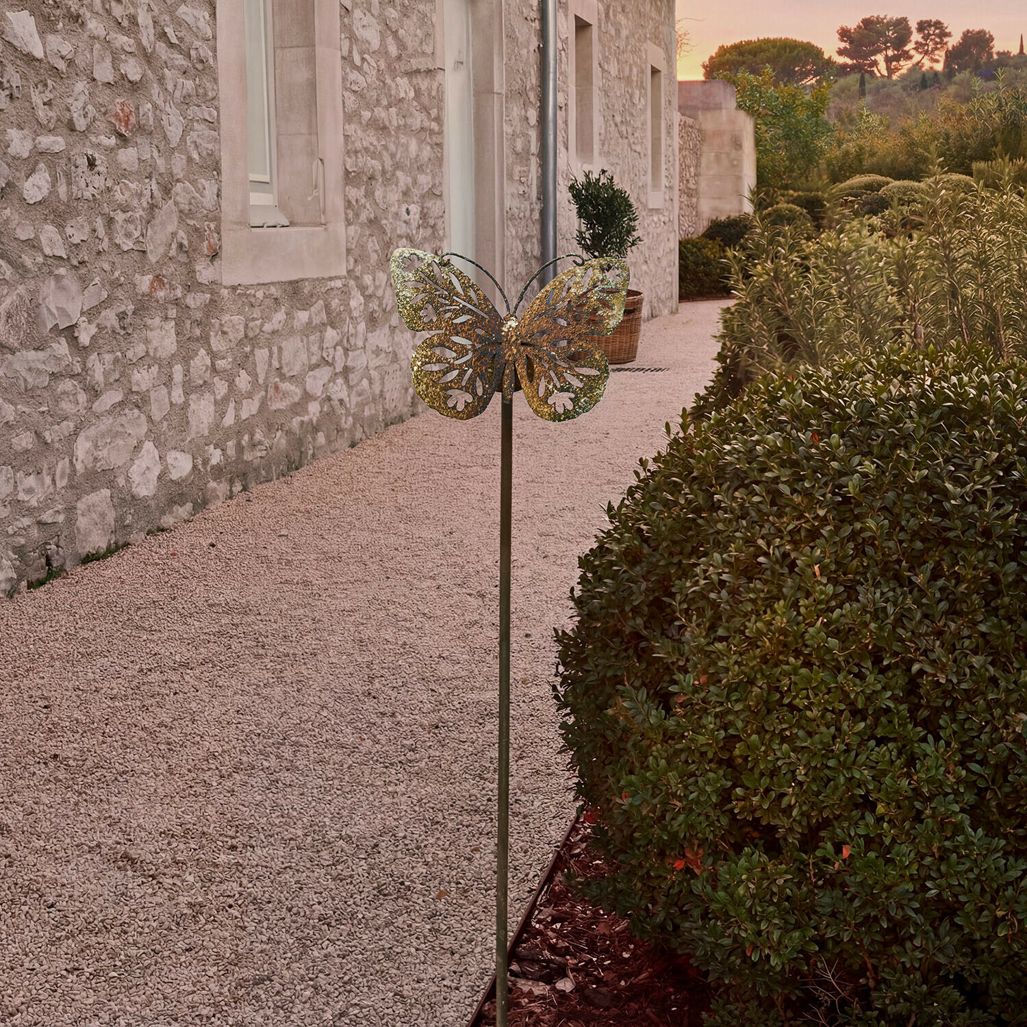 Metalen tuindecoratie in de vorm van een vlinder in messingkleur voor een stenen muur en groenblijvende struiken