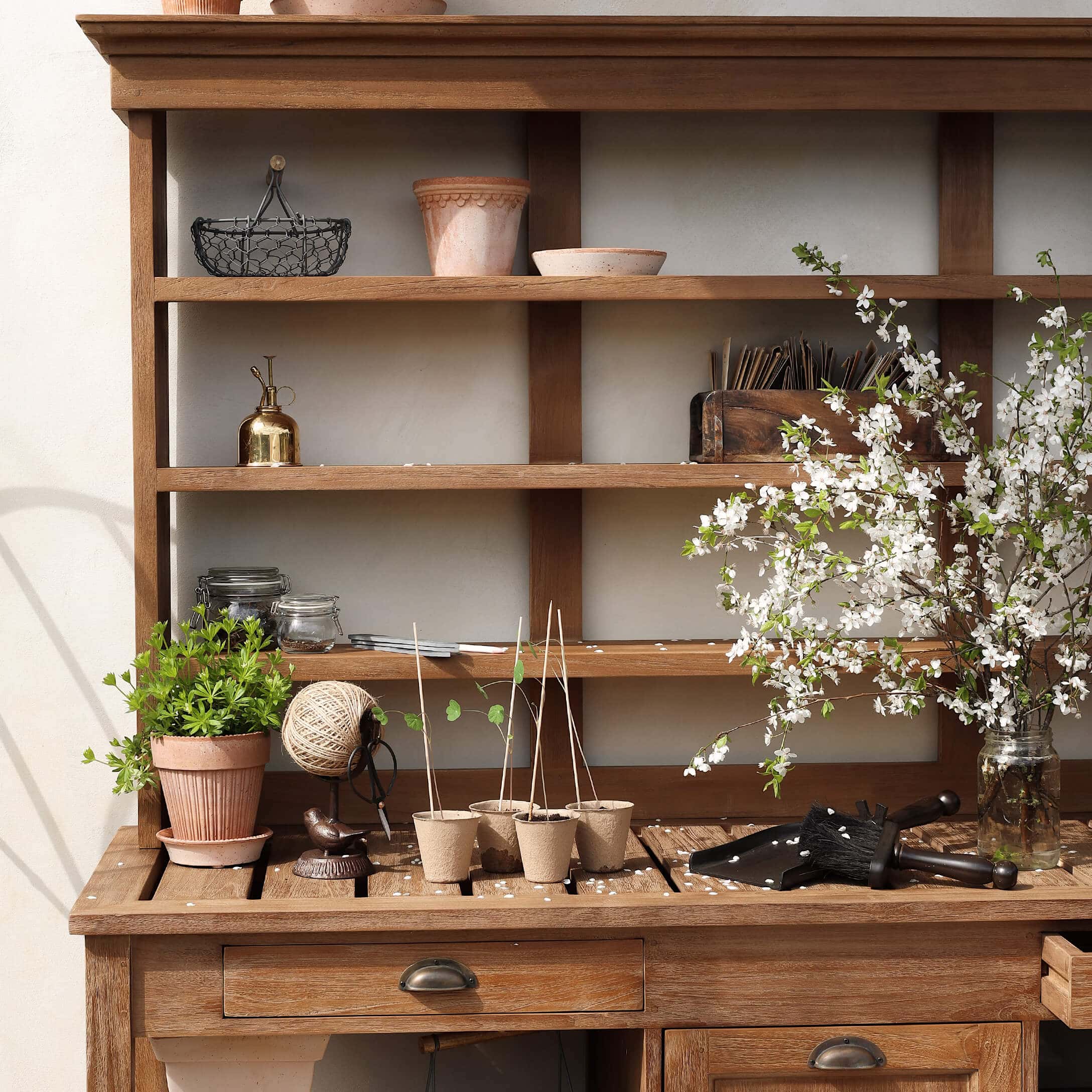 Houten tuintafel met bloempotten, tuingereedschap en bloeiende takken in een glazen pot