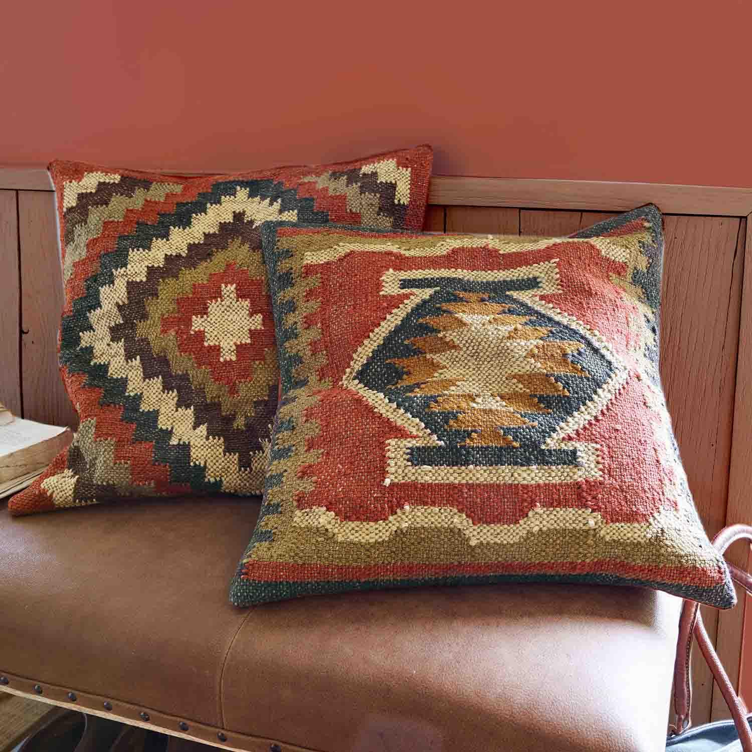 Twee decoratieve kussens van stof met geometrische patronen in warme rood- en beigetinten op een leren bank