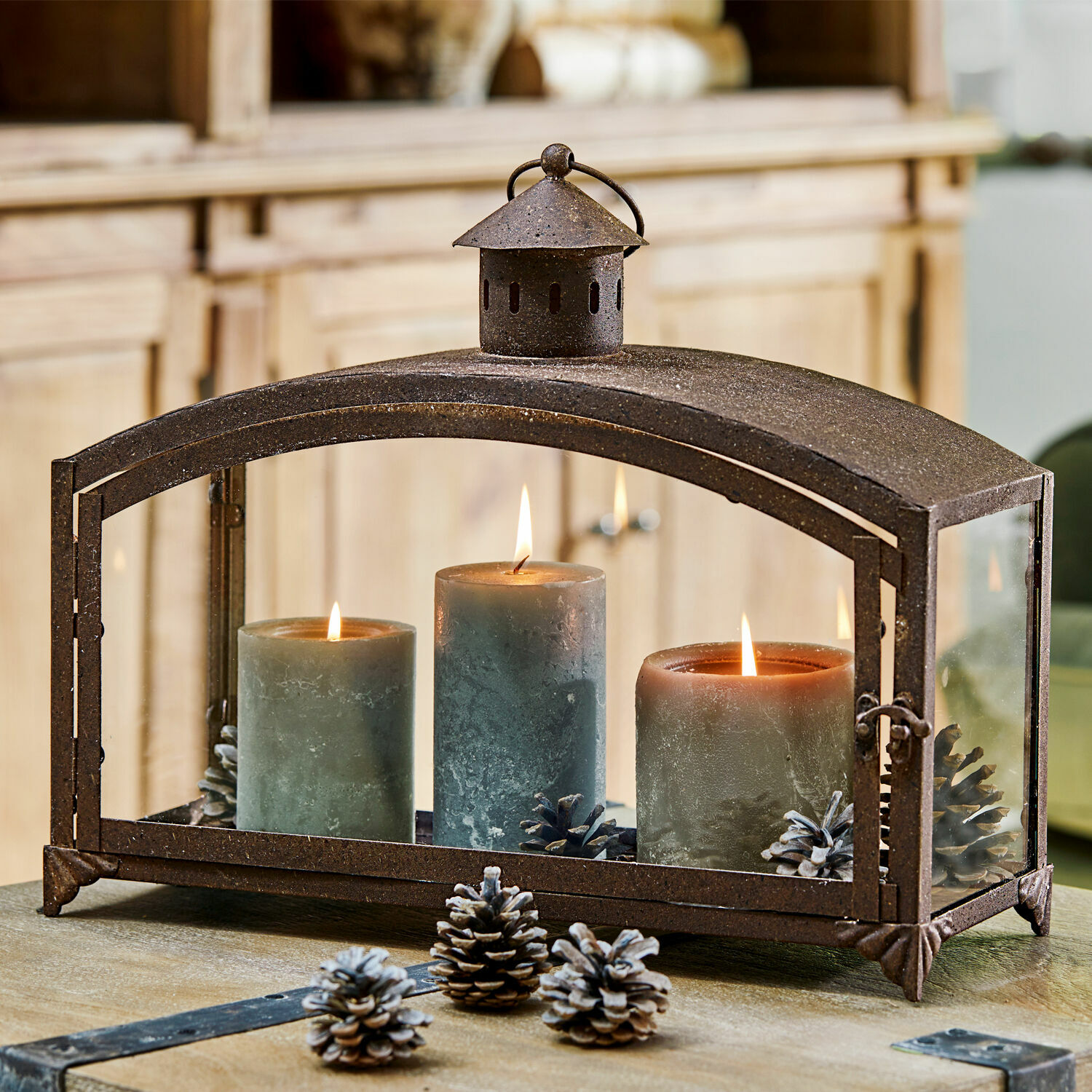 Metalen lantaarn met drie groene kaarsen en dennenappels op houten tafel, interieurdecoratie