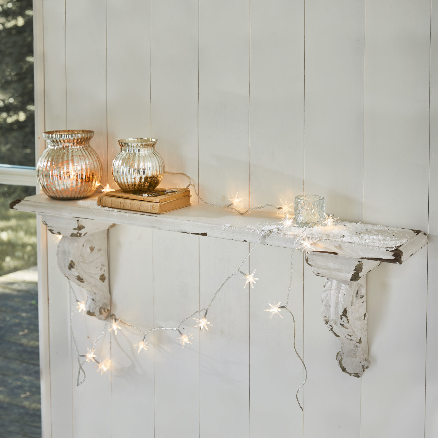 Wandplank Mouscron Witte houten wandplank met verweerde look, versierd met stervormige lichtjes en glazen theelichthouders