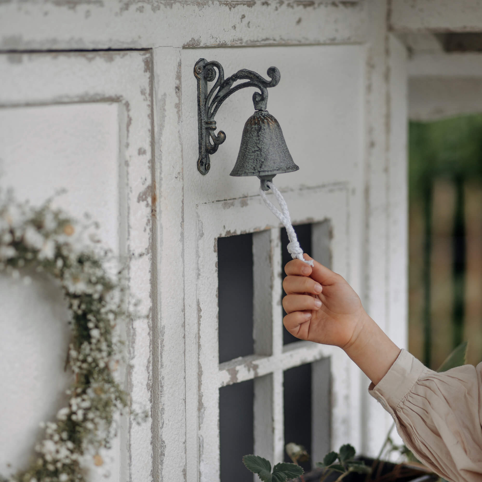 Metalen bel in vintage stijl met wit touw aan verweerde buitenmuur bevestigd