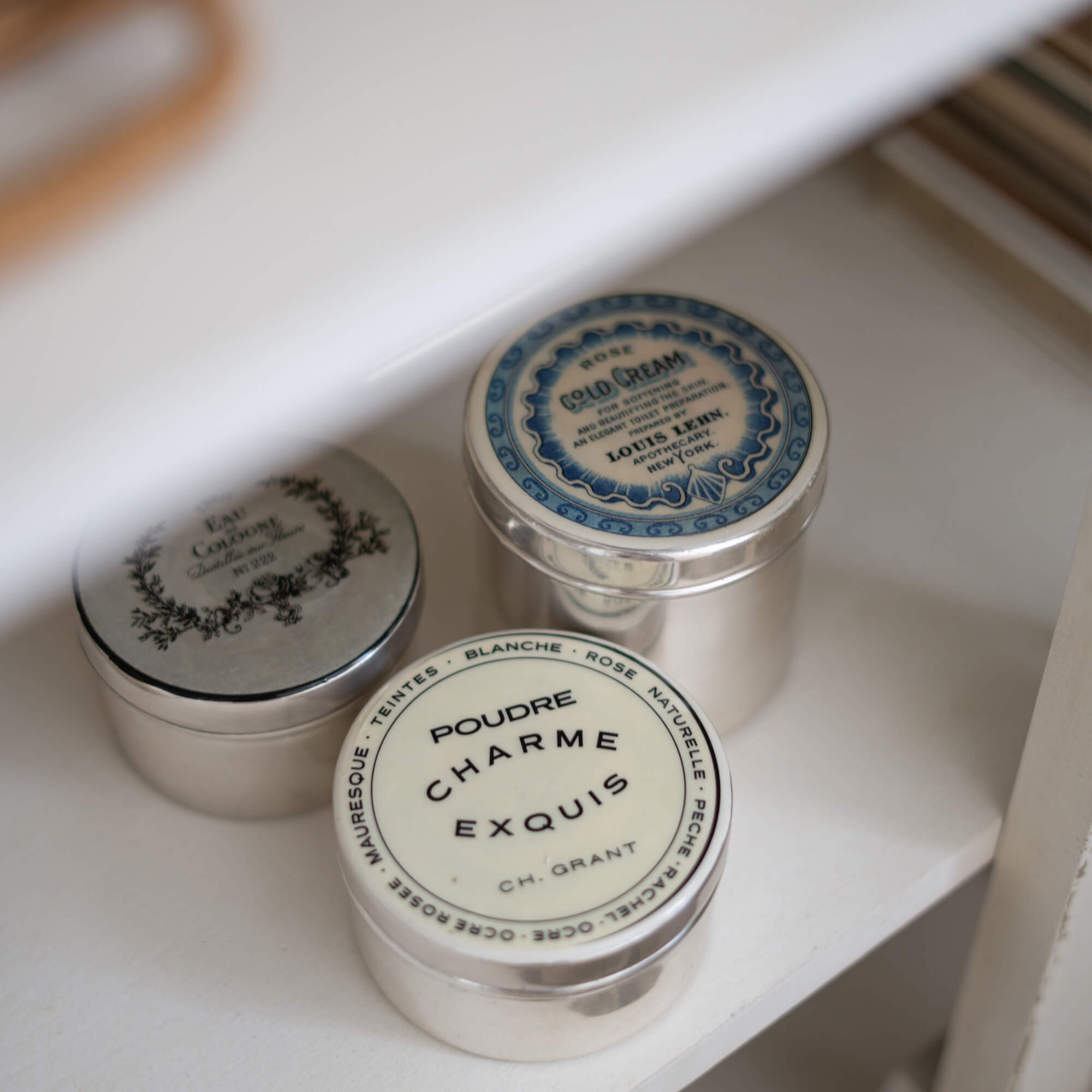 Drie metalen vintage cosmetica potjes op een witte plank voor opslag