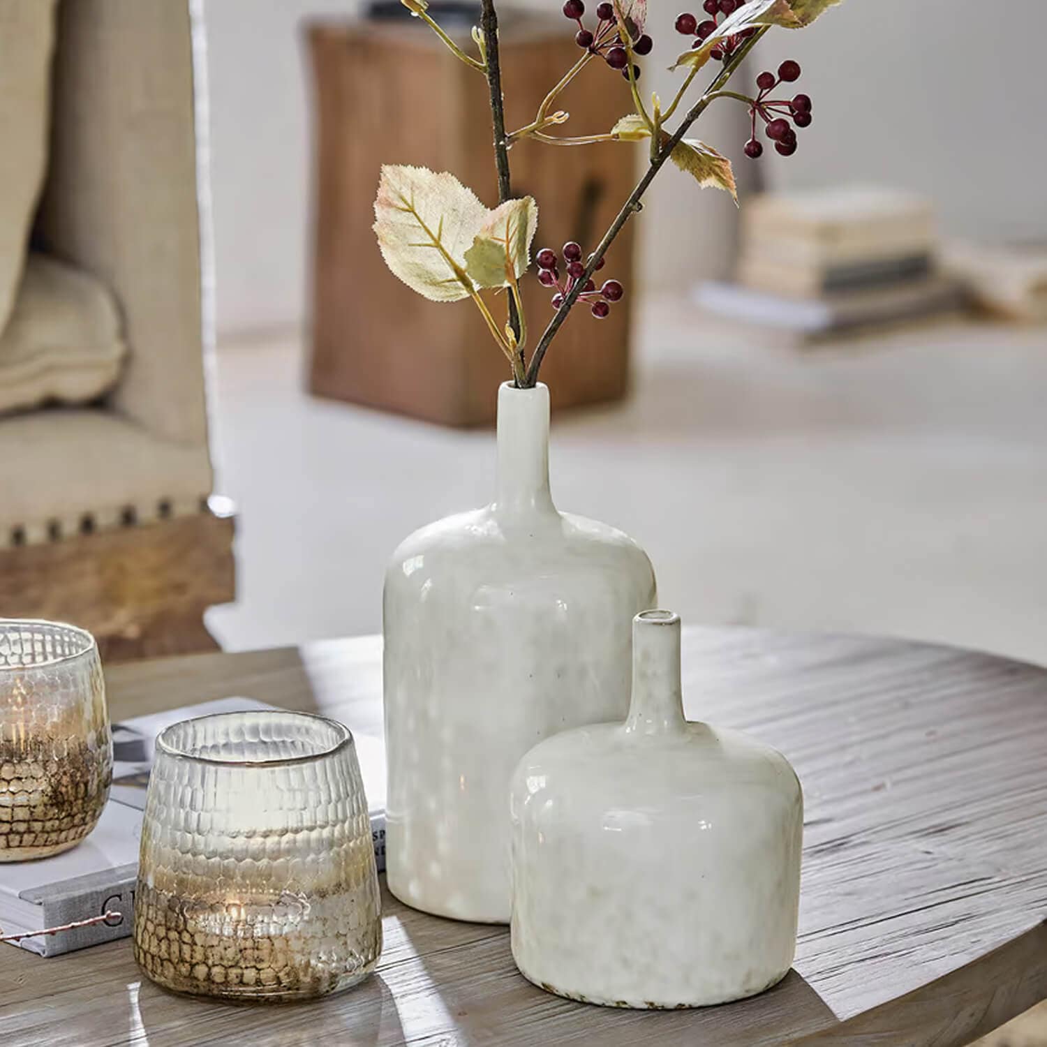 Twee witte keramische vazen op houten tafel met decoratieve takken en kaarsenhouders