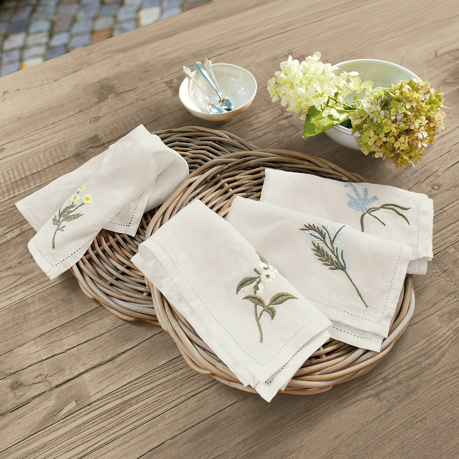 Servet set van 4 Lentilly Linnen servetten met geborduurde plantenmotieven in natuurlijke kleur op een rieten mand op houten tafel