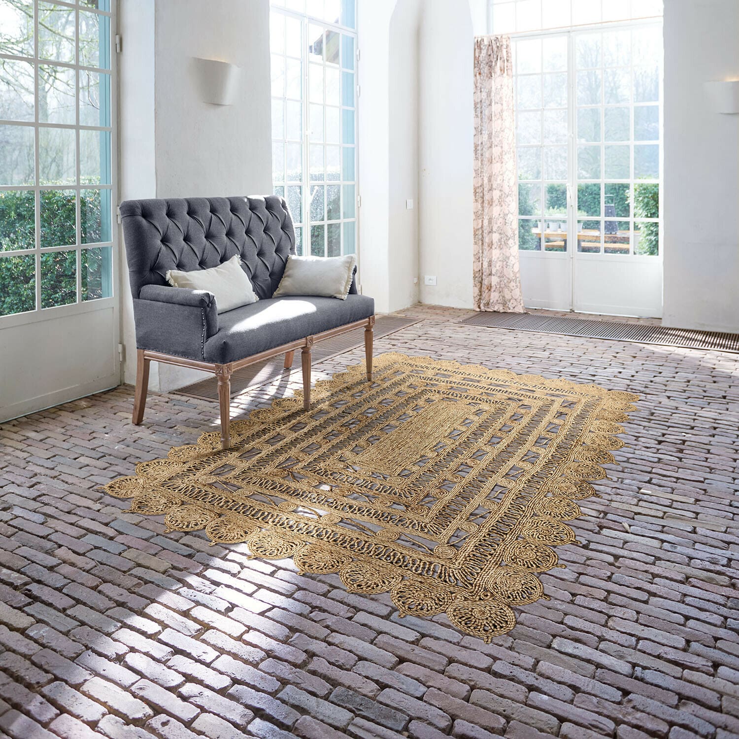 Vloerkleed Livadia Grijze gestoffeerde bank met houten poten in lichte kamer met jute vloerkleed op bakstenen vloer