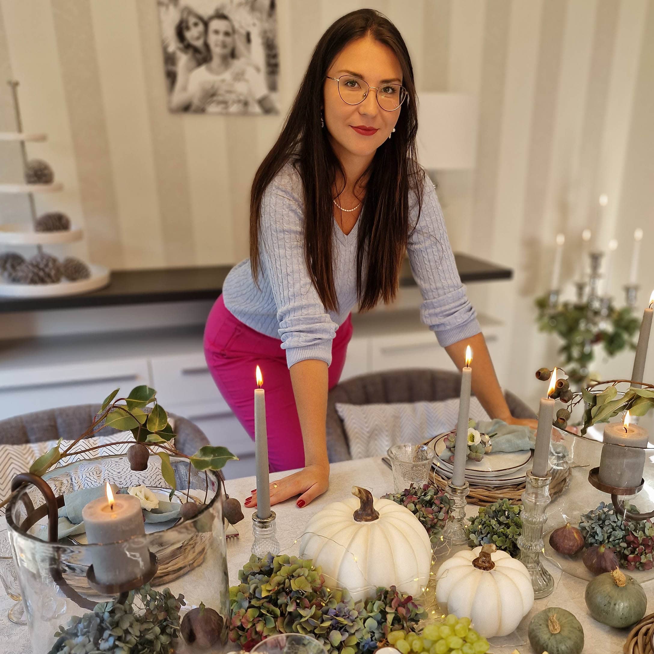 Vrouw bij tafel met herfstdecoratie van witte pompoenen, kaarsen en groene bloemen binnen