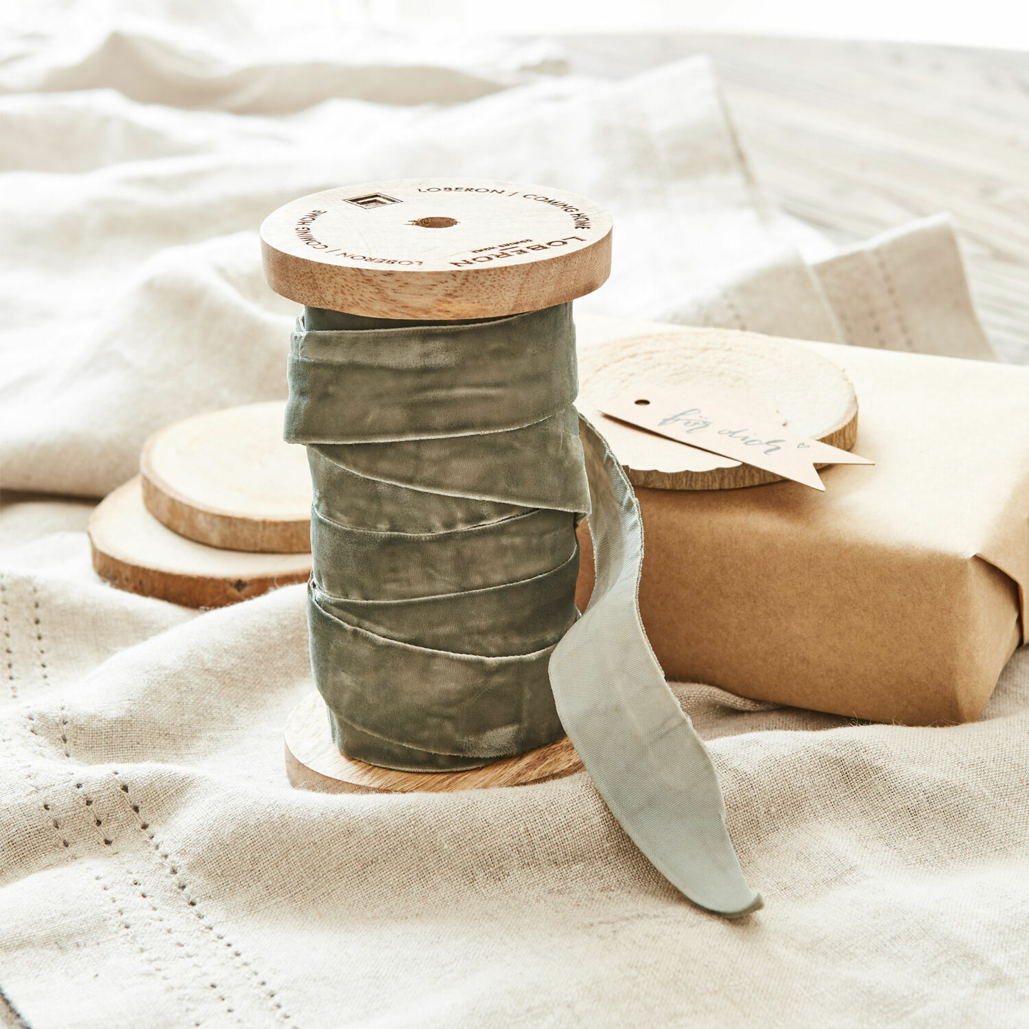 Fluwelen lint Andaris Grijze fluwelen lint op houten spoel op linnen stof met cadeau en label