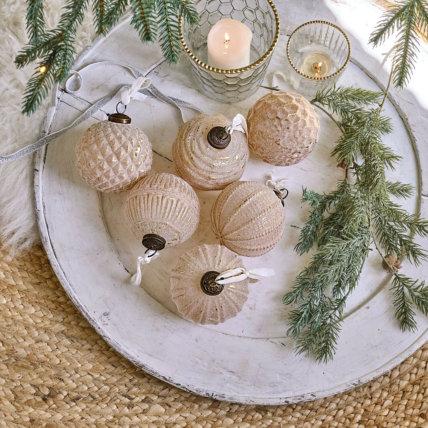Set van zes glazen kerstballen in roségoud op een wit dienblad met dennentakken als decoratie