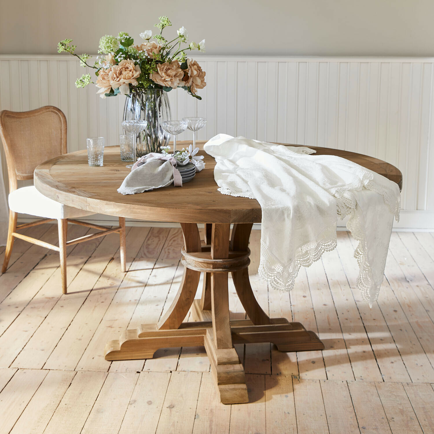 Ronde houten tafel met wit kanten tafelkleed en bloemenboeket in glazen vaas