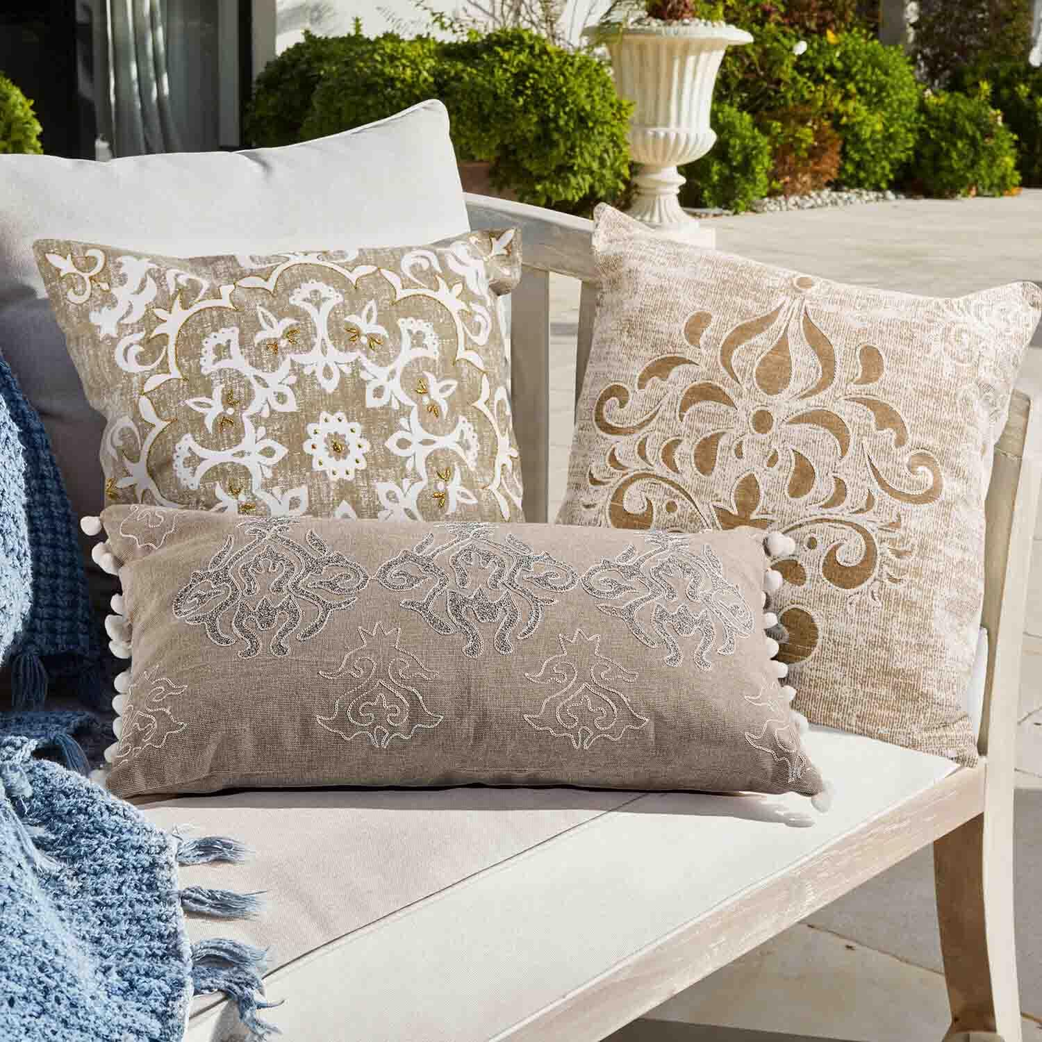 Set van drie decoratieve kussens in beige en wit met patronen op een lichte bank buiten