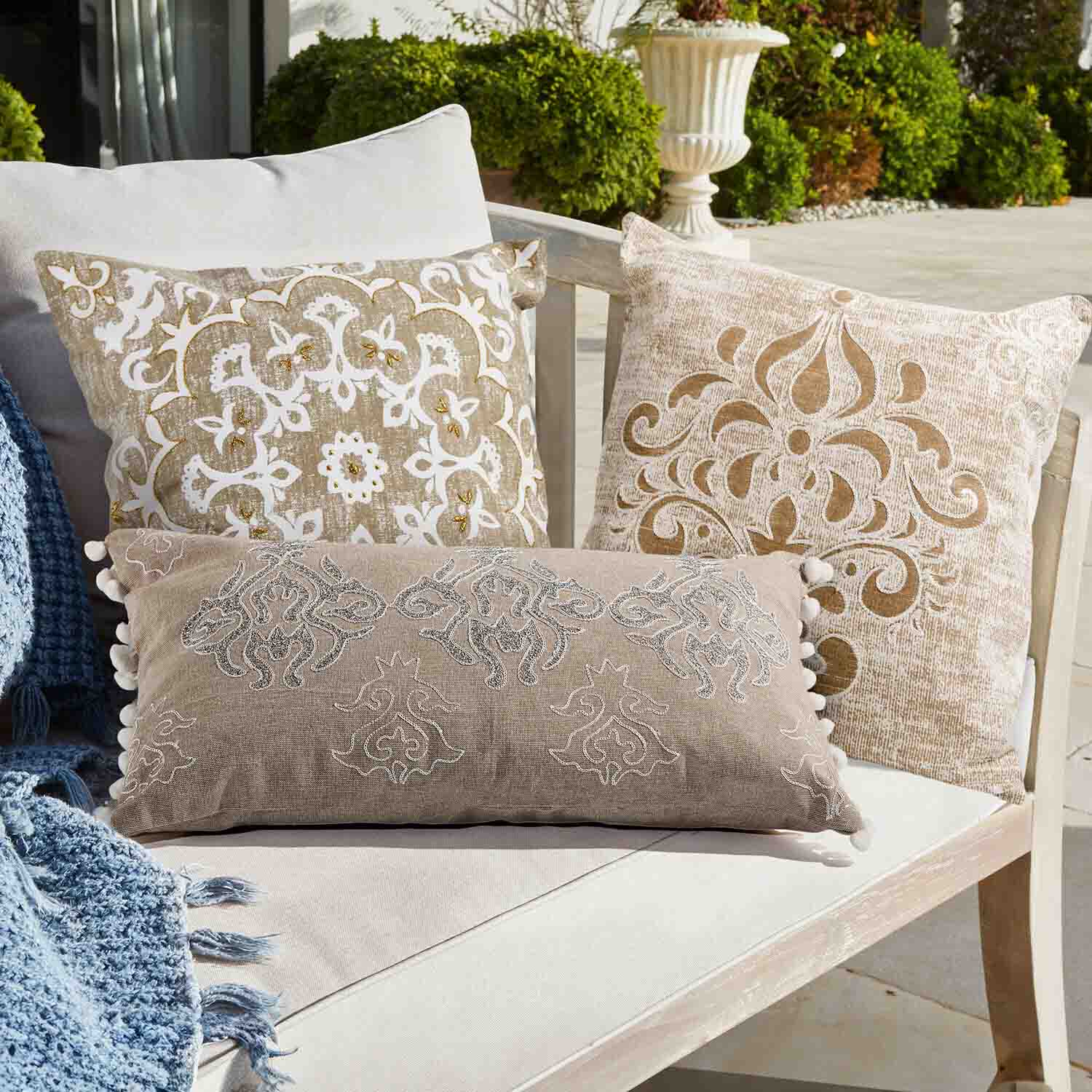 Set van drie decoratieve kussens in beige en wit met patronen op een lichte bank buiten