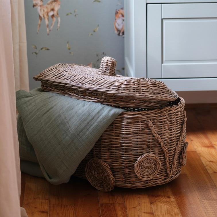 Rieten mand in autovorm met groene deken op houten vloer in kinderkamer