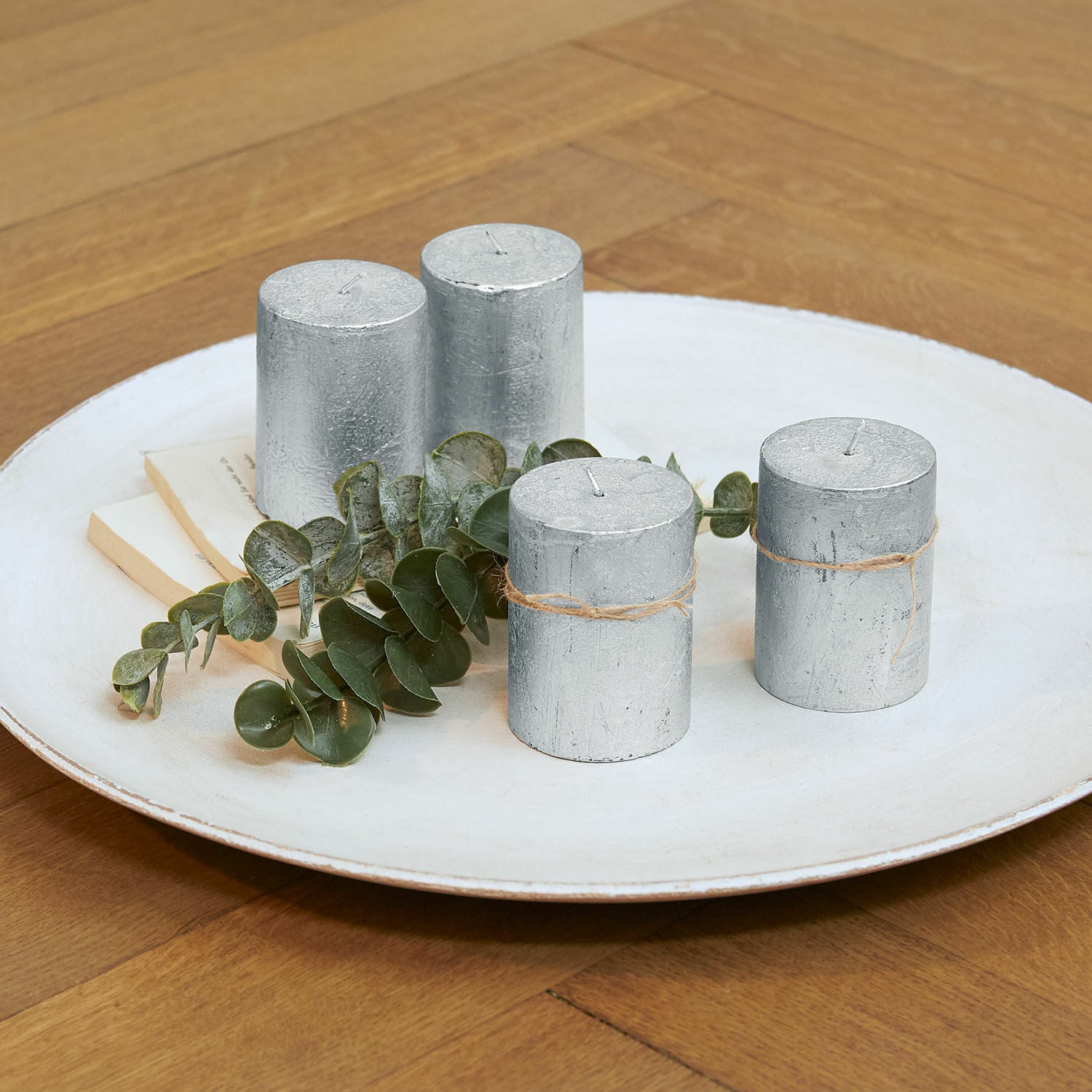 Kaars set van 4 Virrans Set van vier zilverkleurige cilindervormige kaarsen met juten touw op een wit bord met groene bladeren