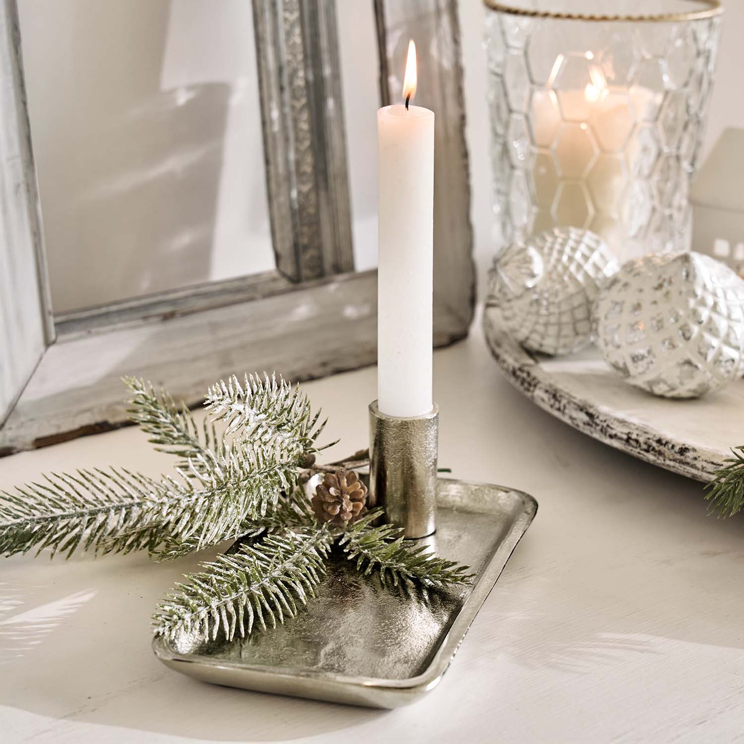 Zilverkleurige metalen kandelaar met witte kaars en dennentakdecoratie op lichte tafel