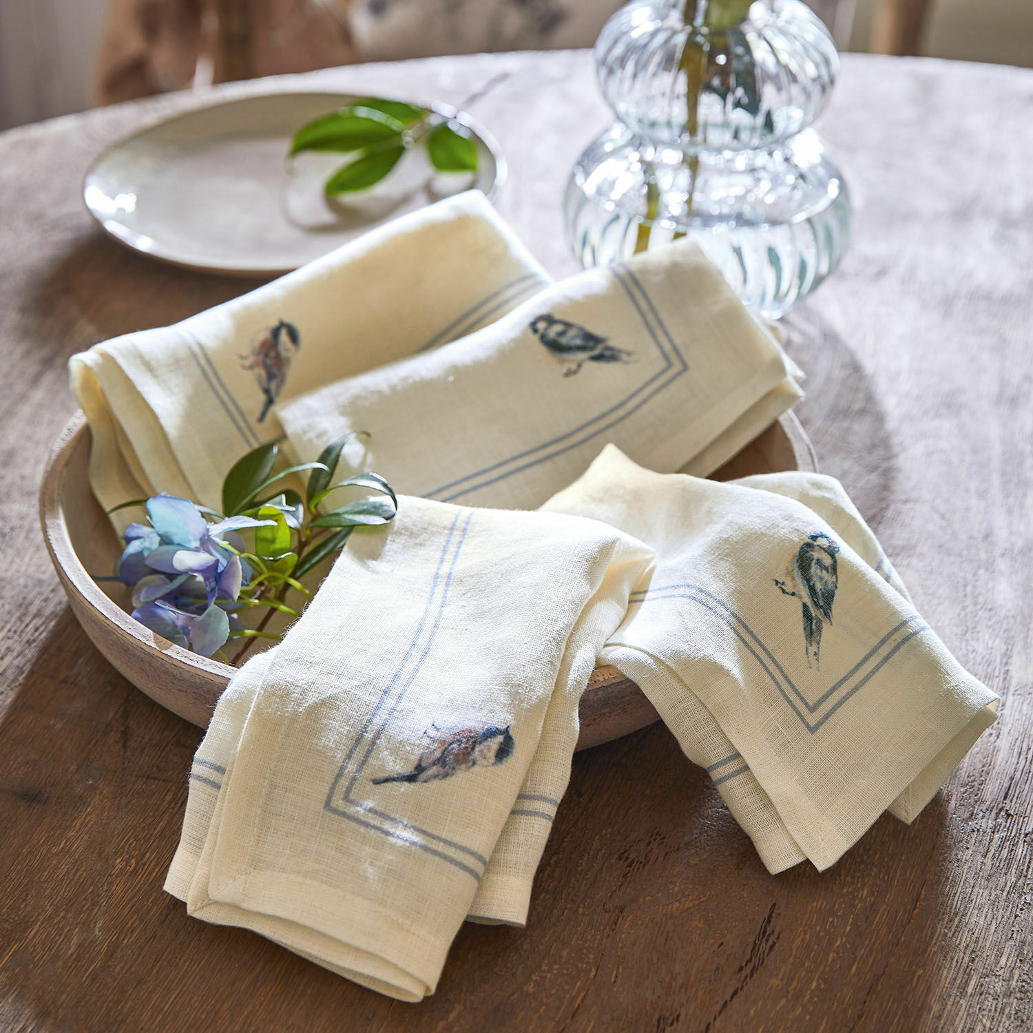Crèmekleurige linnen servetten met vogelprint op houten schaal, rustieke tafeldecoratie